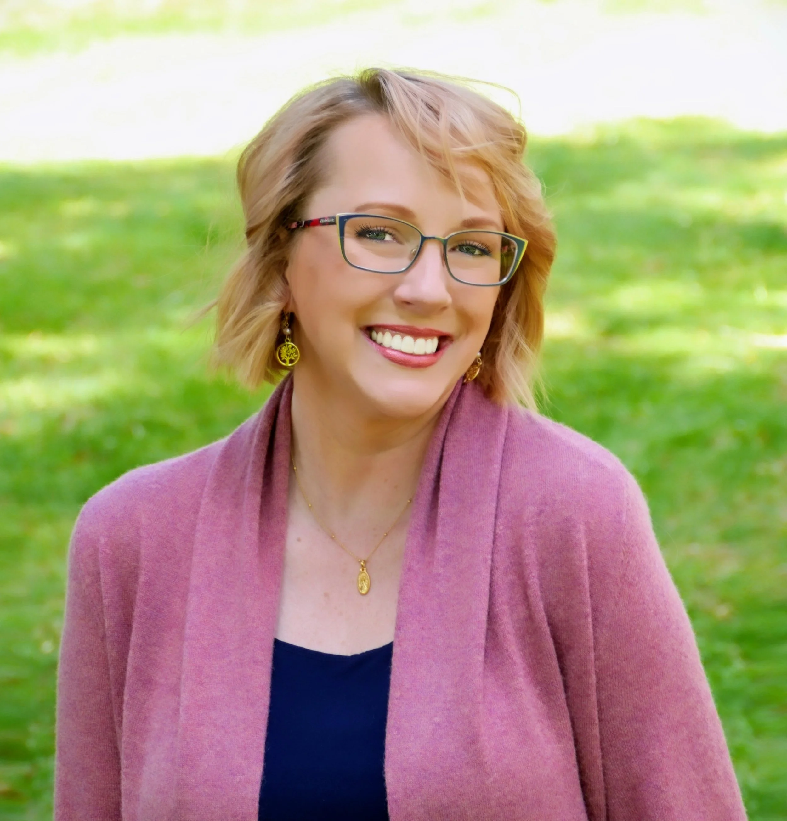 Smiling blonde woman wearing glasses and a pink blazer outdoors