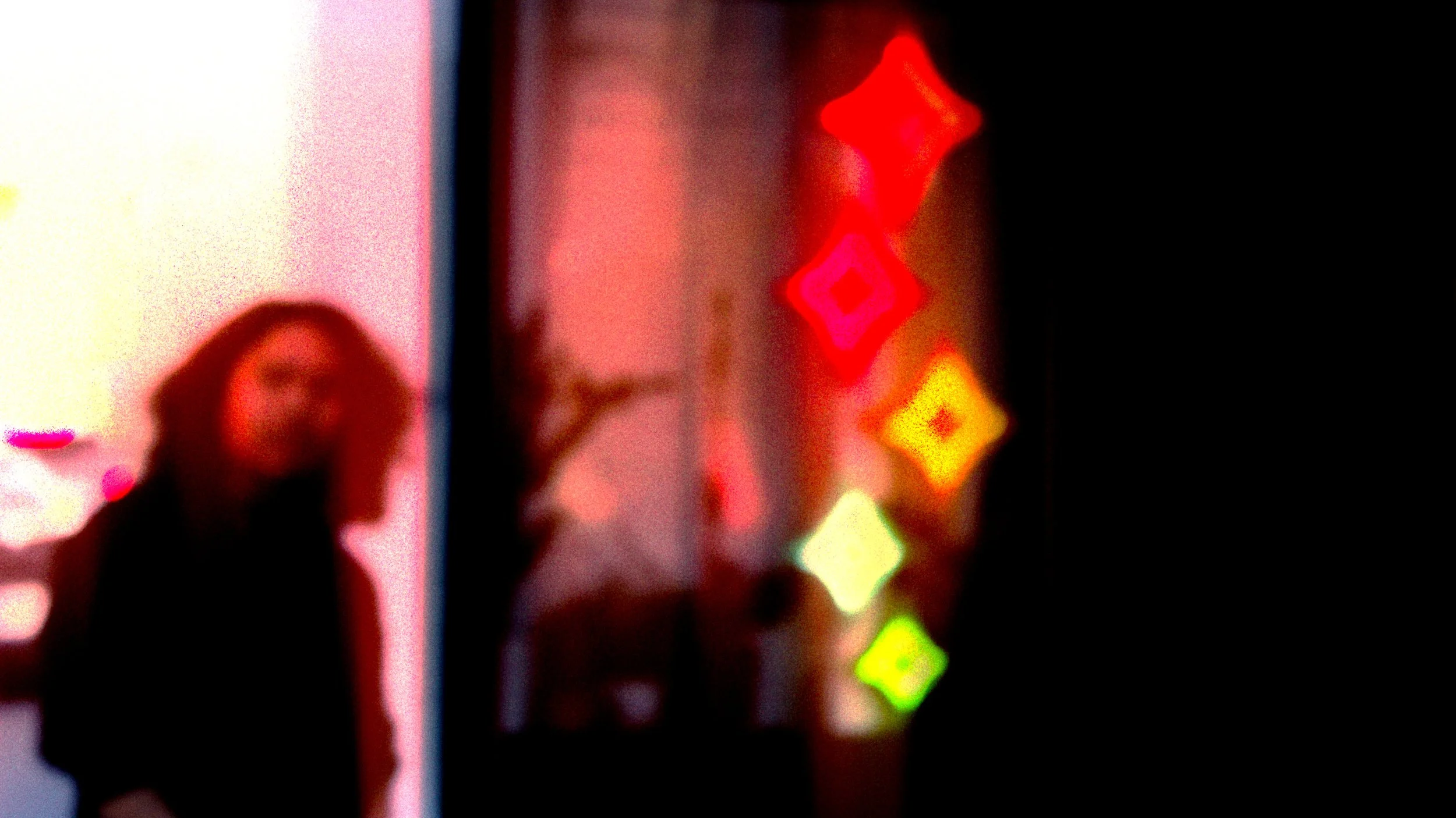 Blurred image of a person taking a selfie in front of a colorful, illuminated background with diamond-shaped lights.