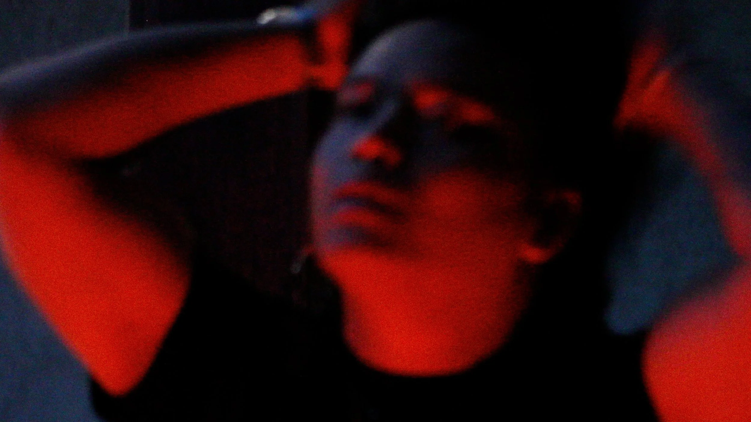 A blurred close-up image with dark and red tones, possibly showing parts of human hands or objects.
