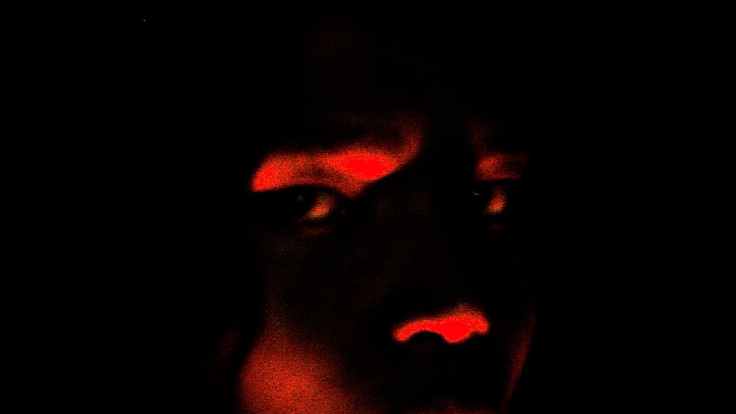 A dark image with red and orange light reflections on a face, partially visible, creating an abstract appearance.