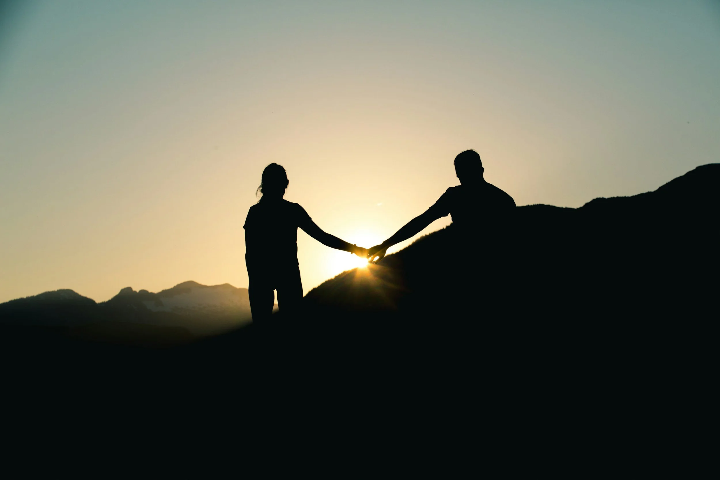 couple holding hands light peeking through at the top of a peak