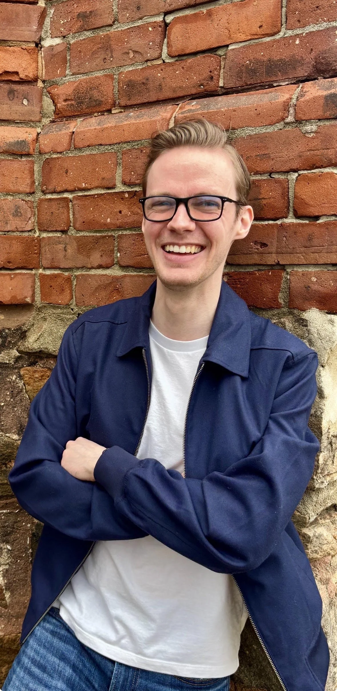 Male Intern Student Therapist - Bryn Robinson smiling at camera wearing a blue jacket in front of a red bricked building.