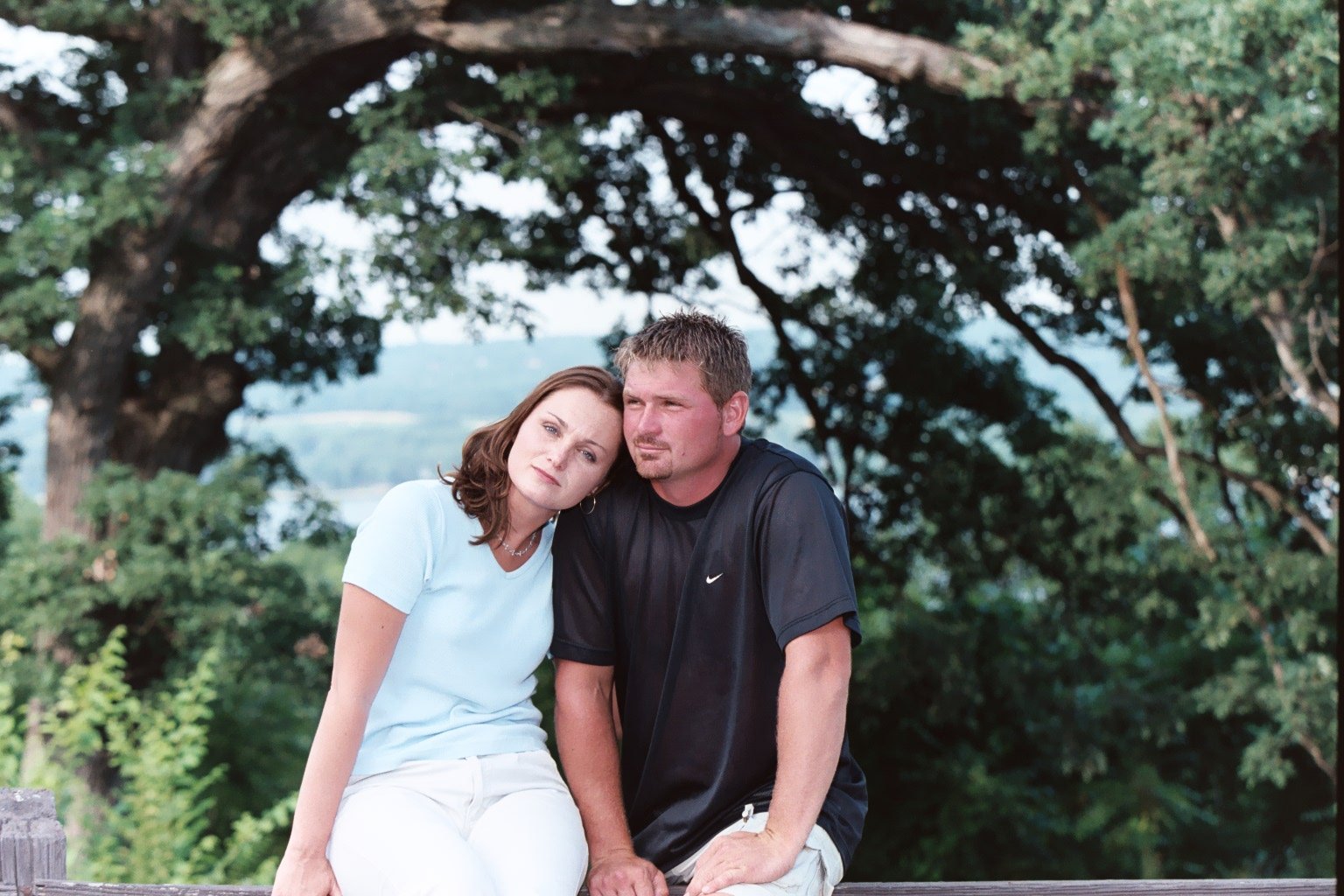 Woman in blue tee shirt rests her head on the shoulder of a man in a black tee shirt.