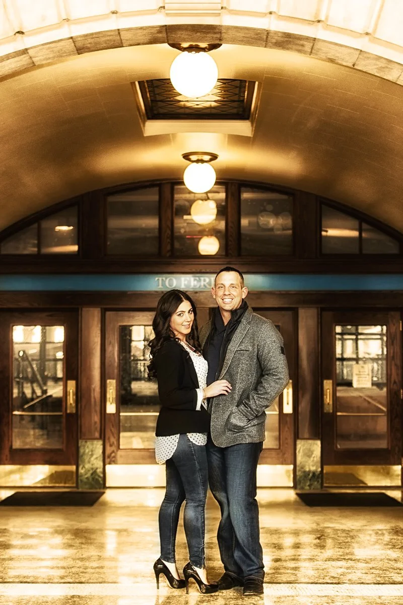 Woman with long dark hair stands close to a man in a tweed jacket, both are smiling.