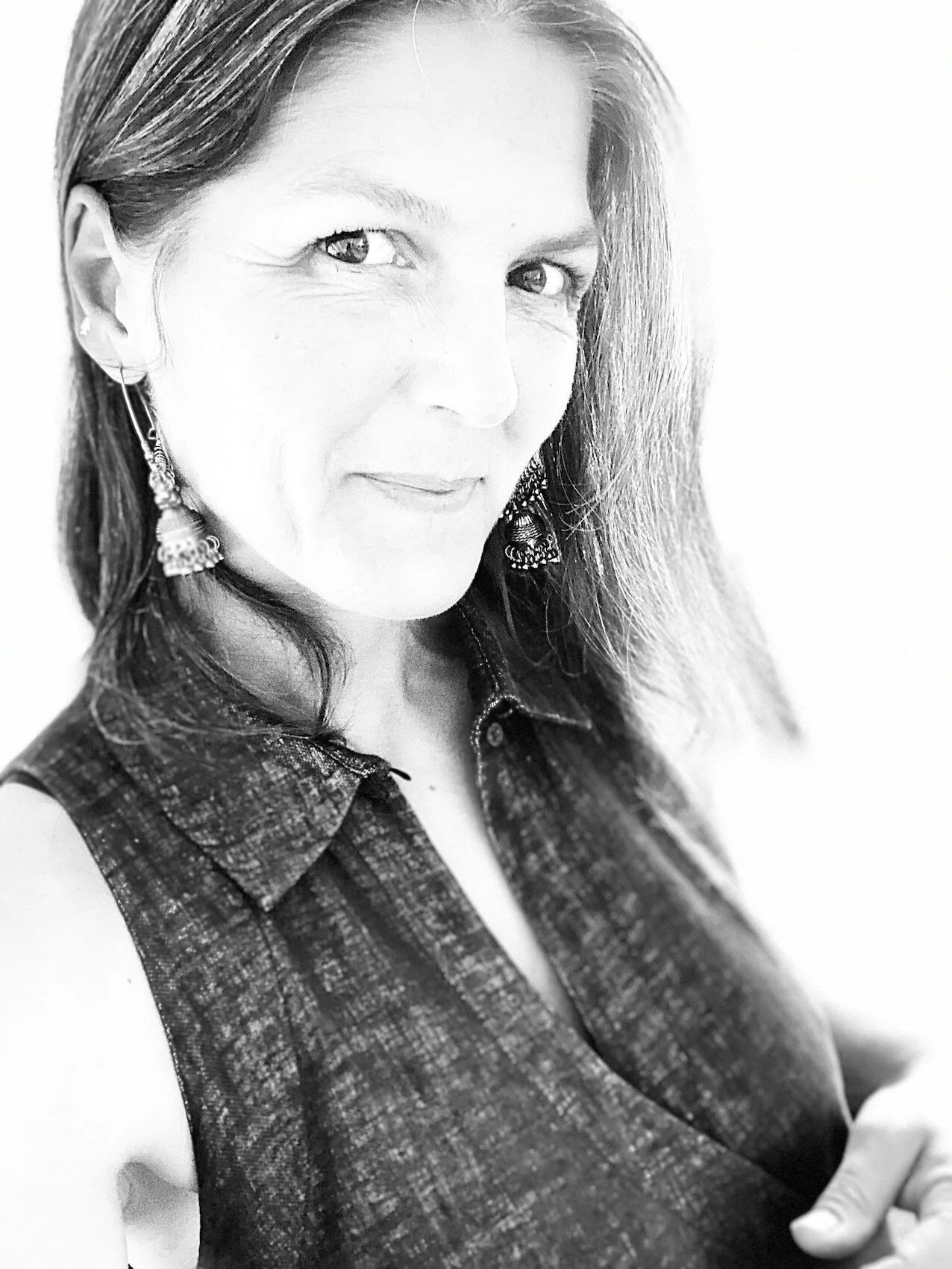 Black and white portrait of a person smiling, wearing dangly earrings and a sleeveless top.