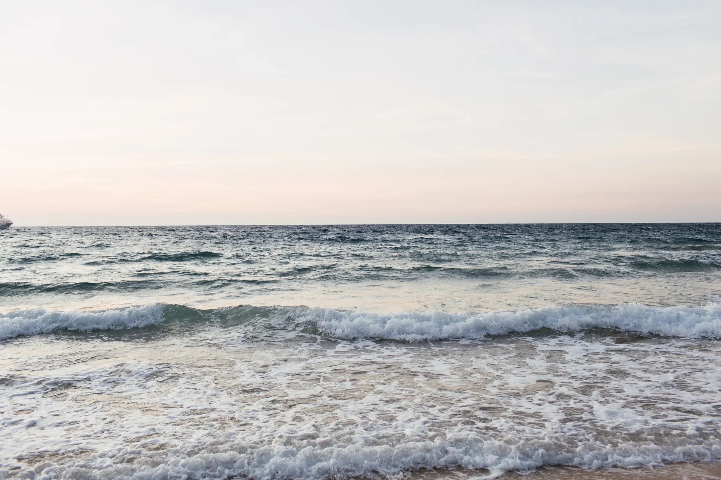 Calm ocean waves at sandy beach during sunrise.