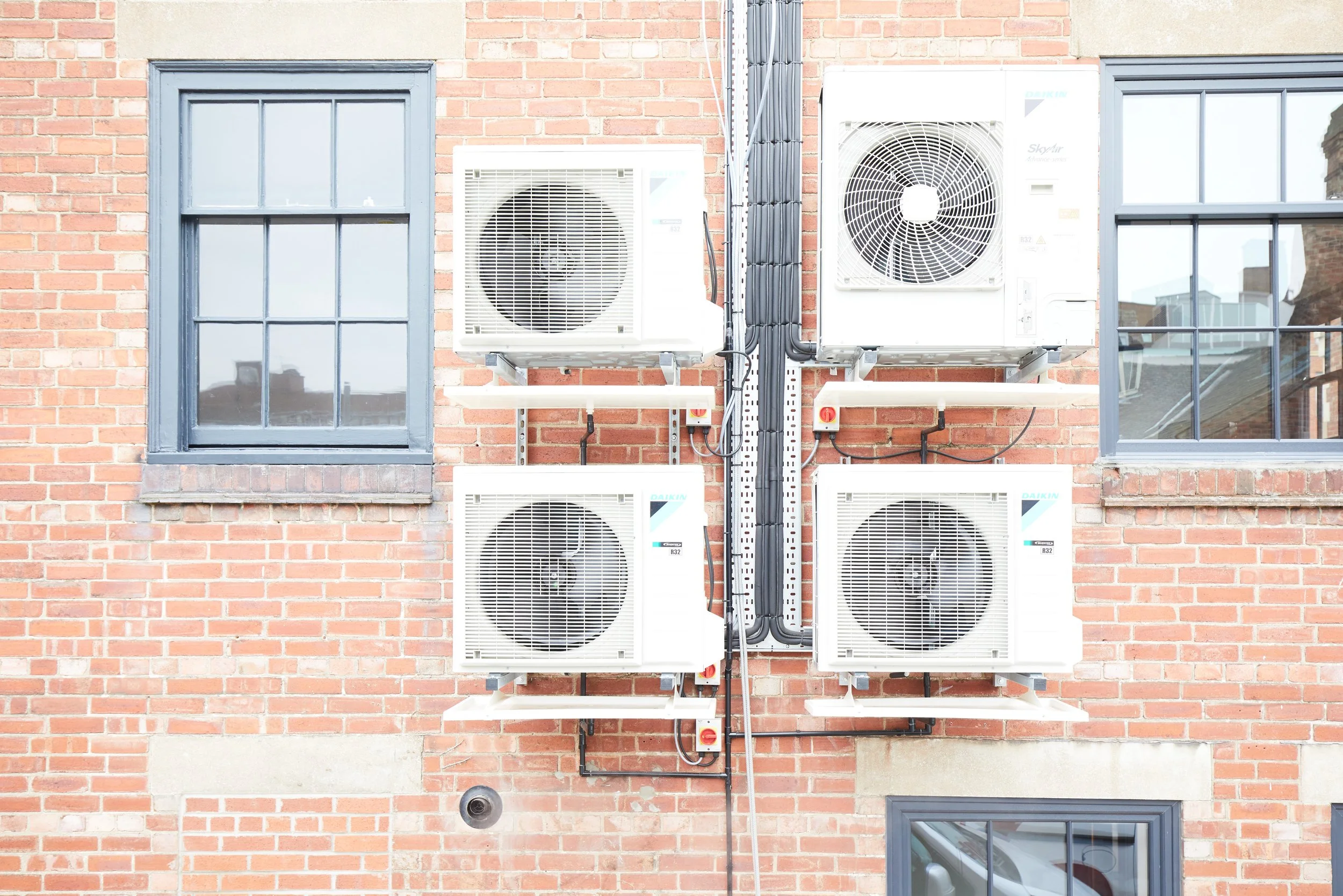 Air conditioning units mounted on a brick building wall with windows.
