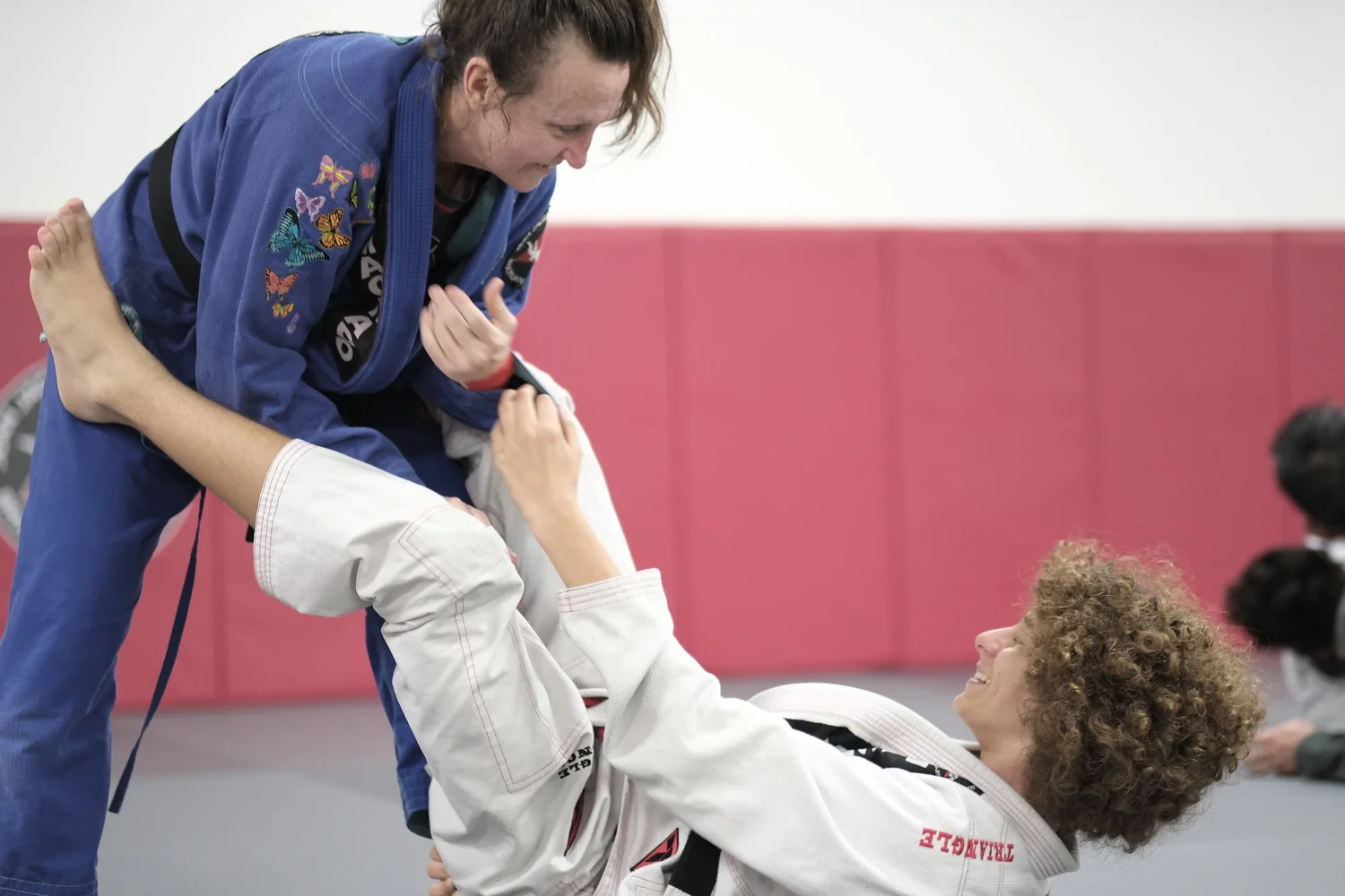 Two students training jiu jitsu, one in a blue gi and one in a white gi