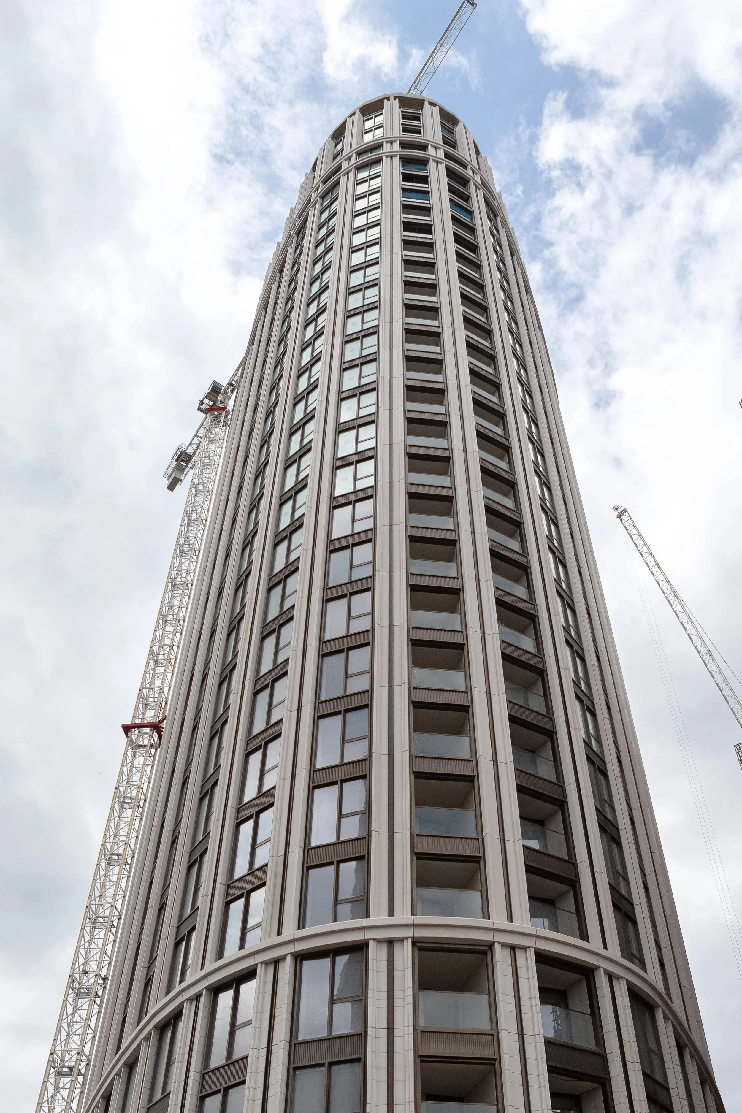 Tall modern building under construction with cranes against a cloudy sky.