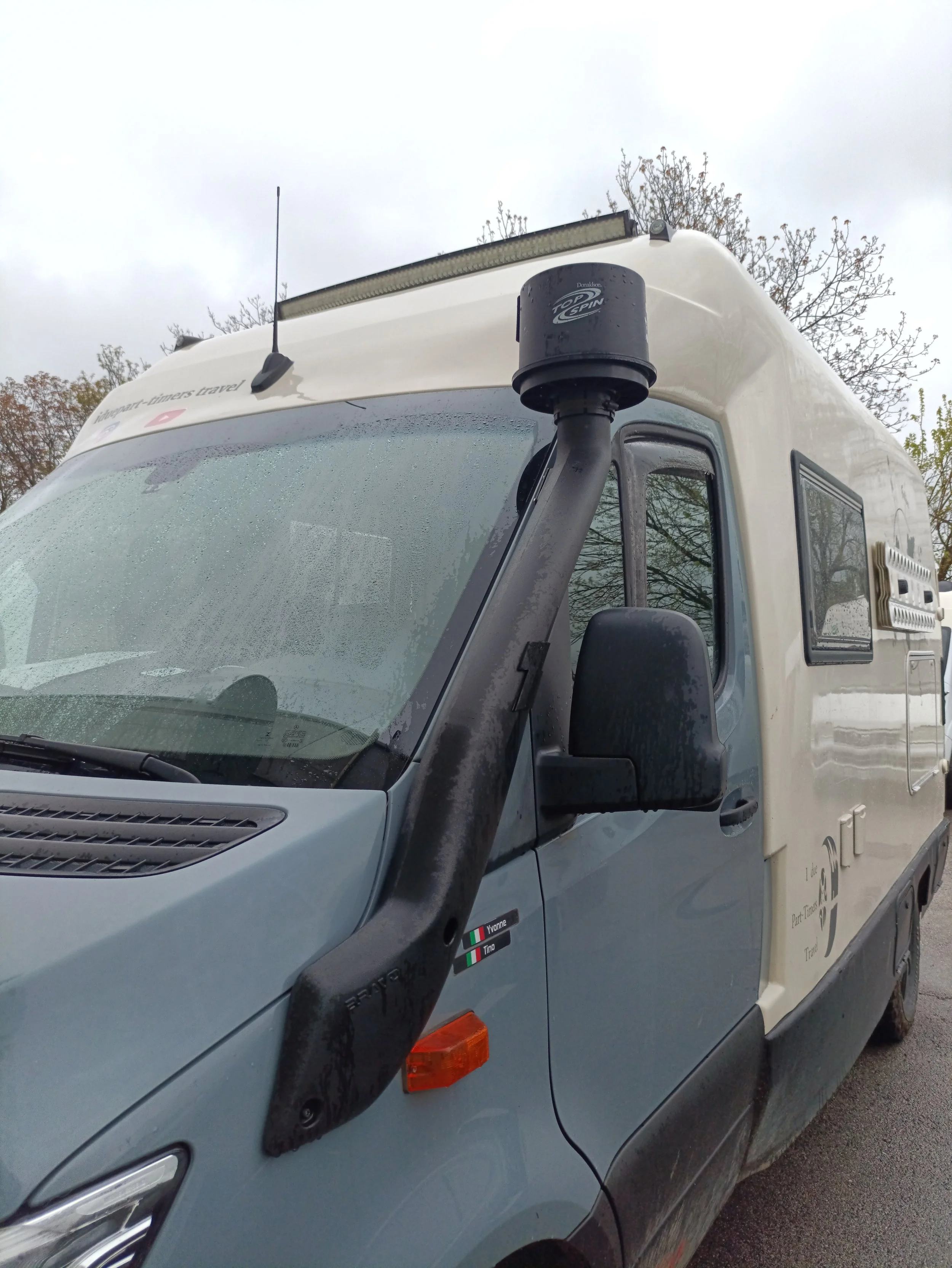 Furgoncino con snorkel nero sulla fiancata, logo di viaggio per appunti di viaggio, e piccoli adesivi con le bandiere di Italia e Ungheria.