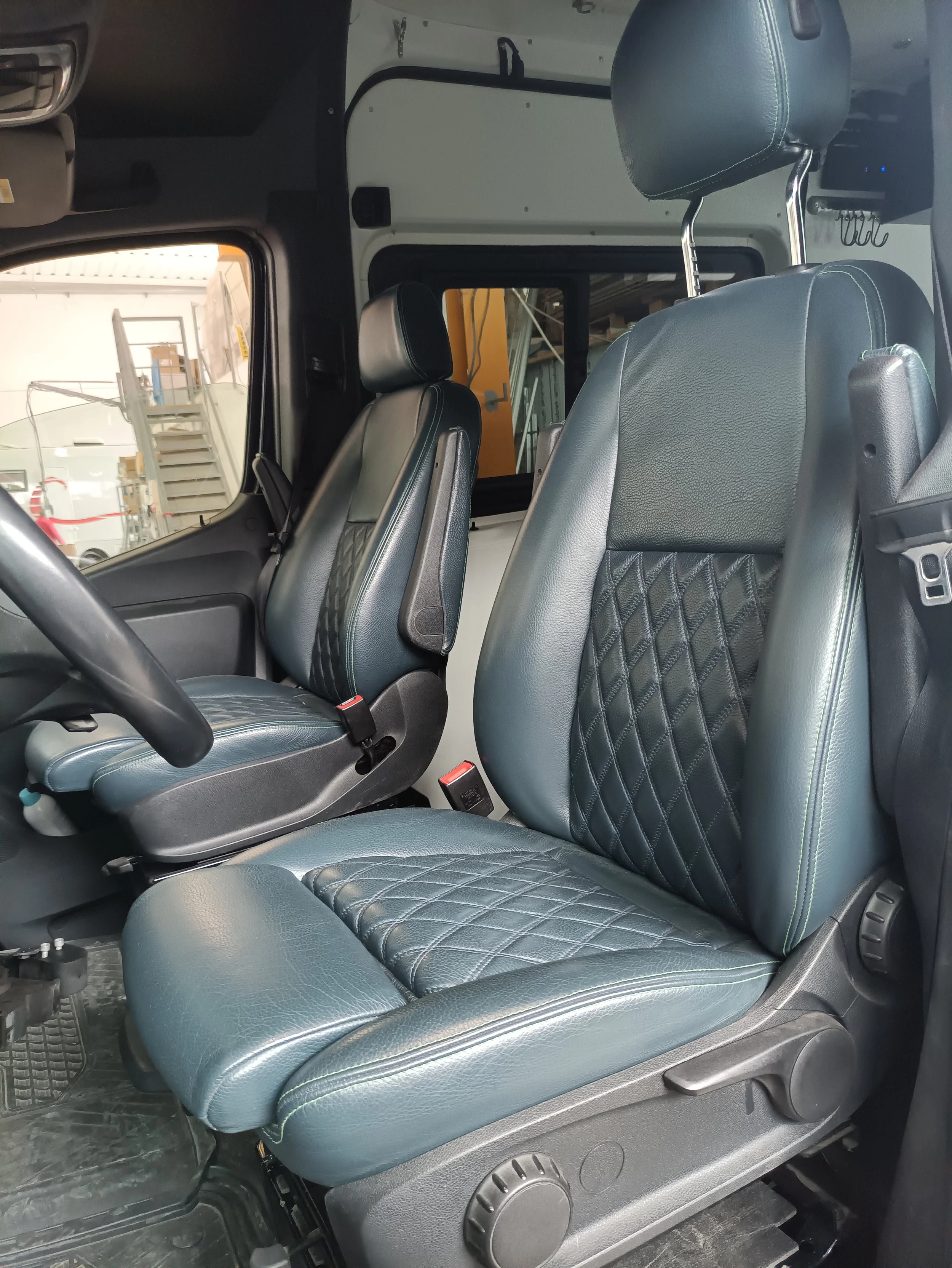 Interior di un veicolo con due sedili di pelle blu, uno davanti e uno dietro, in un magazzino
