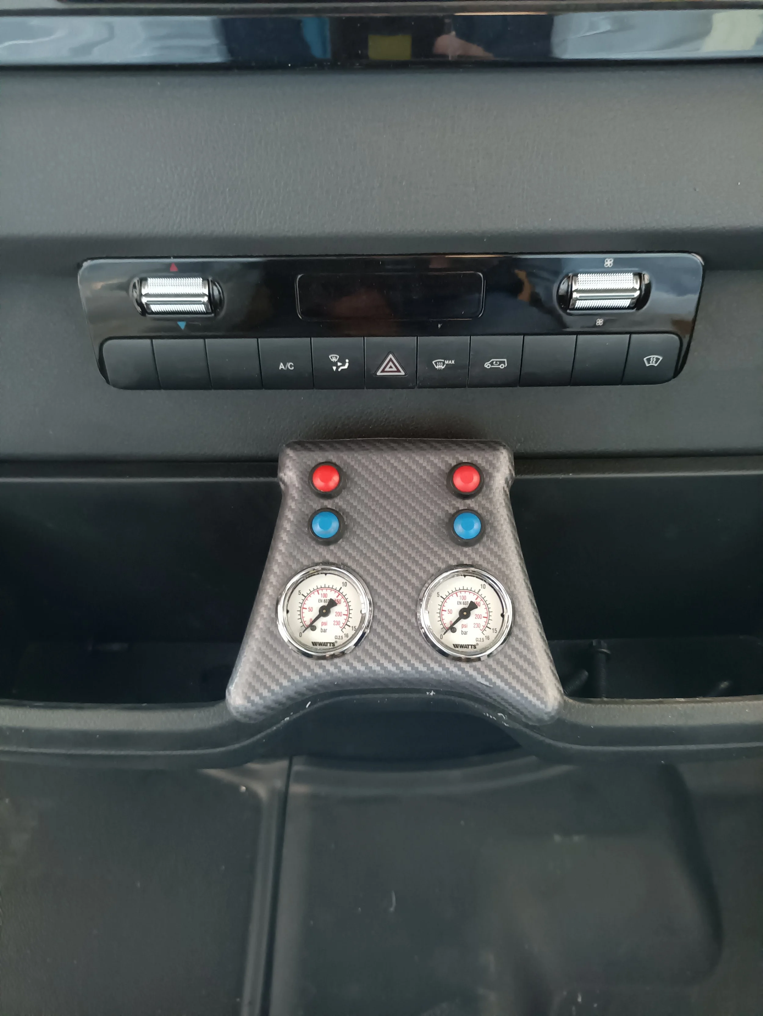 Pannello di controllo di un'auto con comandi di clima e due manometri con tubi rossi e blu.