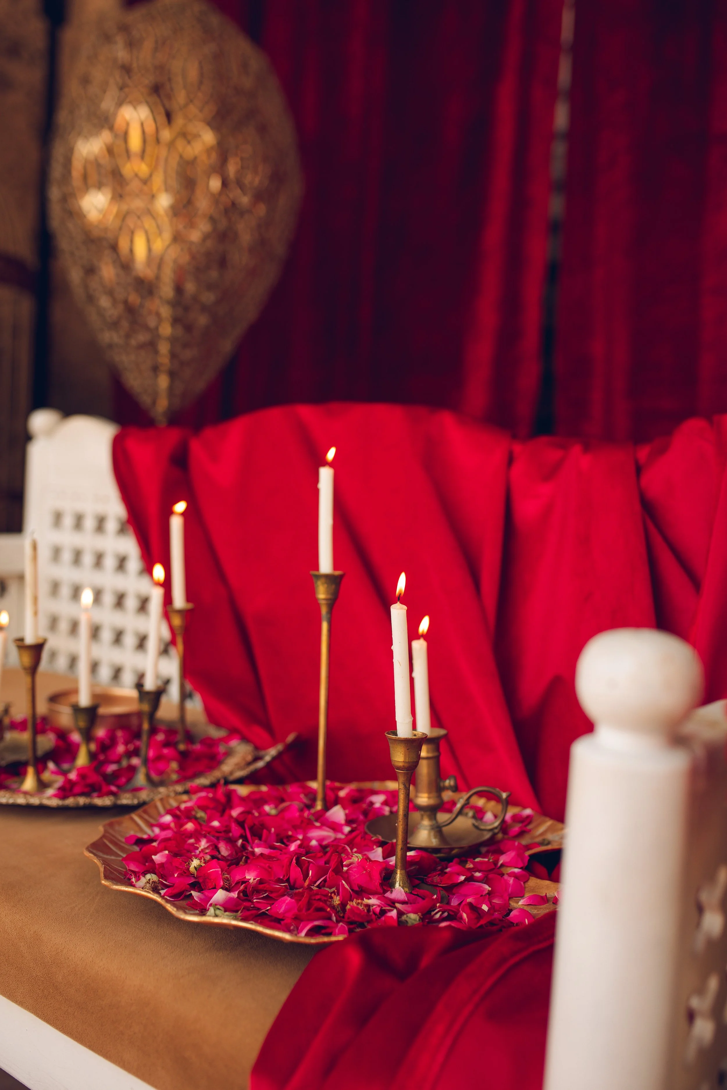 Romantic setting with lit candles, rose petals, and red drapery on a decorative tray against a rich red fabric backdrop.