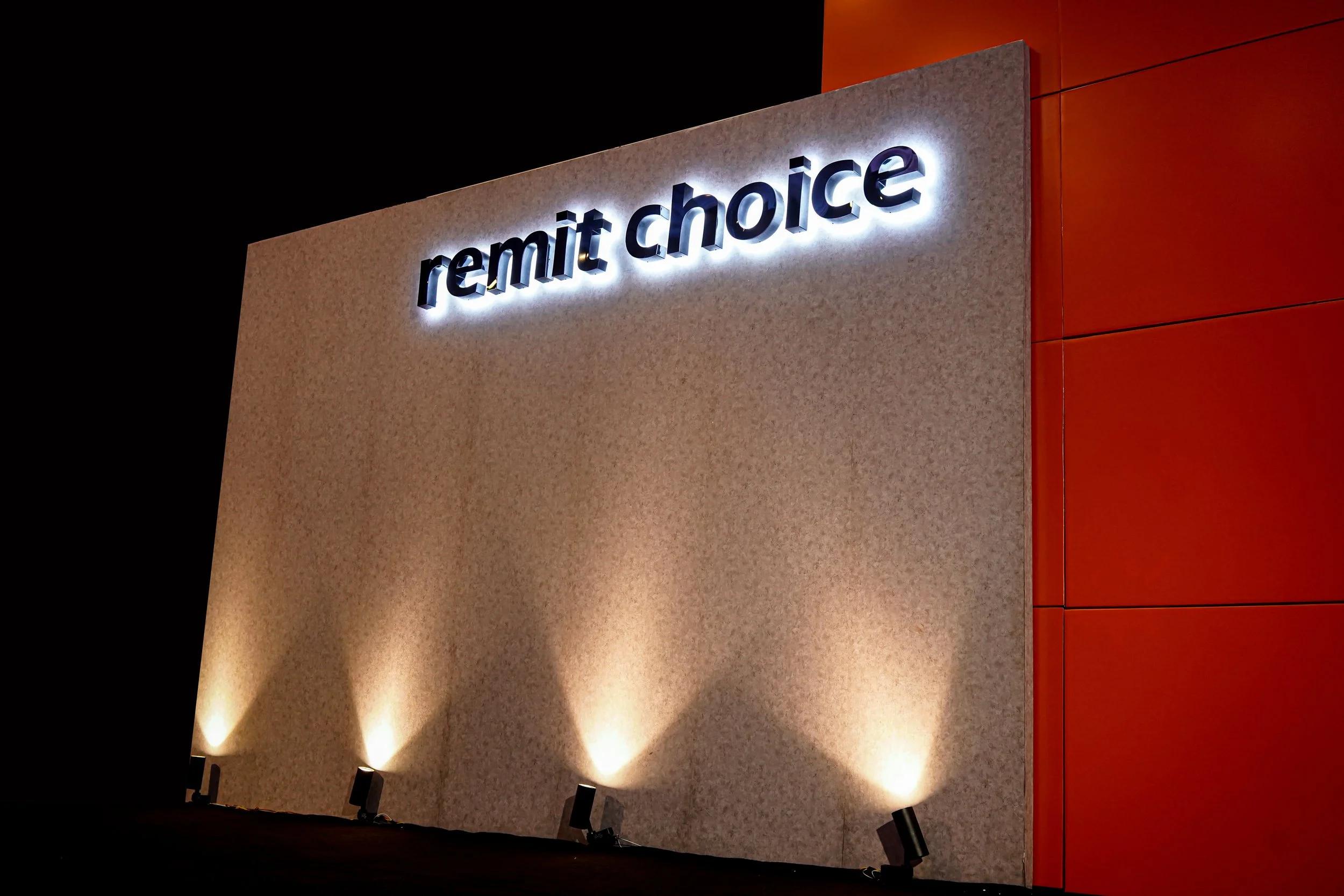 Illuminated sign with 'remit choice' on a wall with spotlights below.