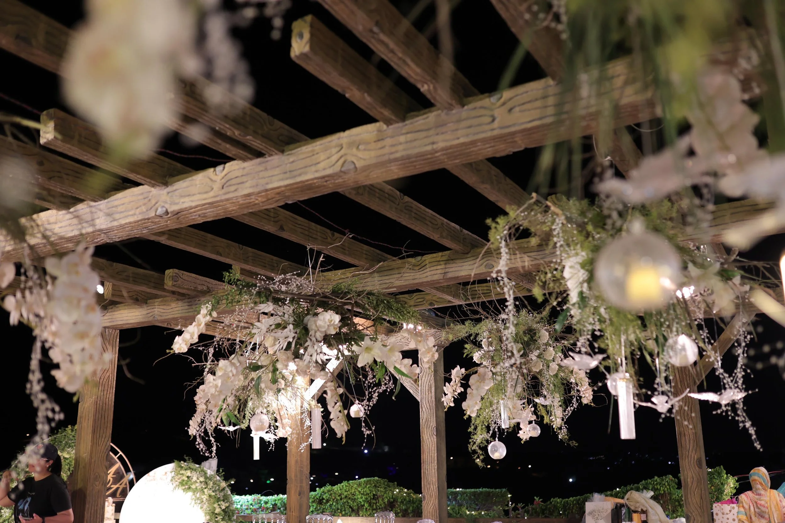 Outdoor pergola decorated with white flowers and glass ornaments at night