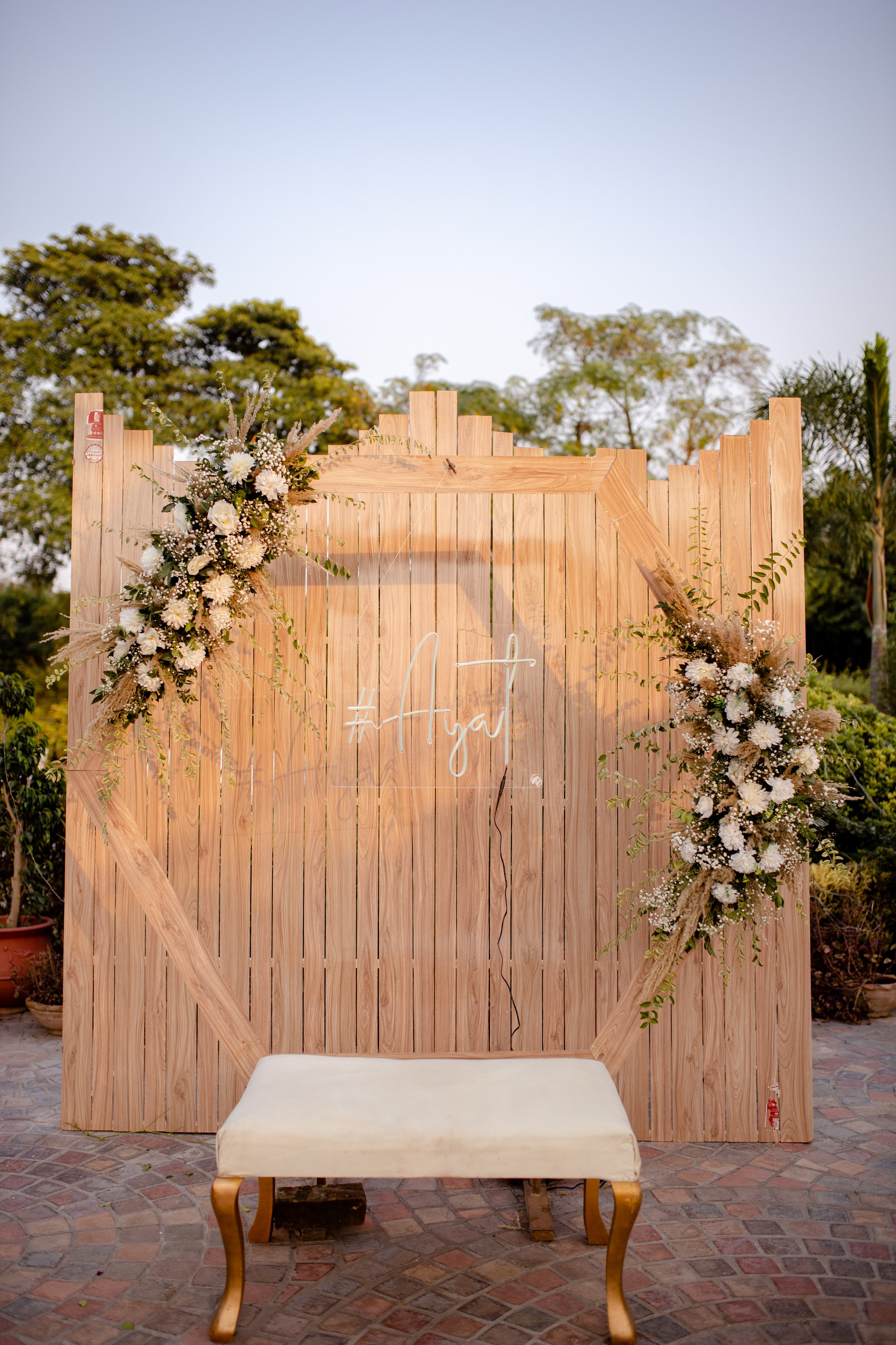 Outdoor wooden backdrop with floral arrangements and a decorative bench.
