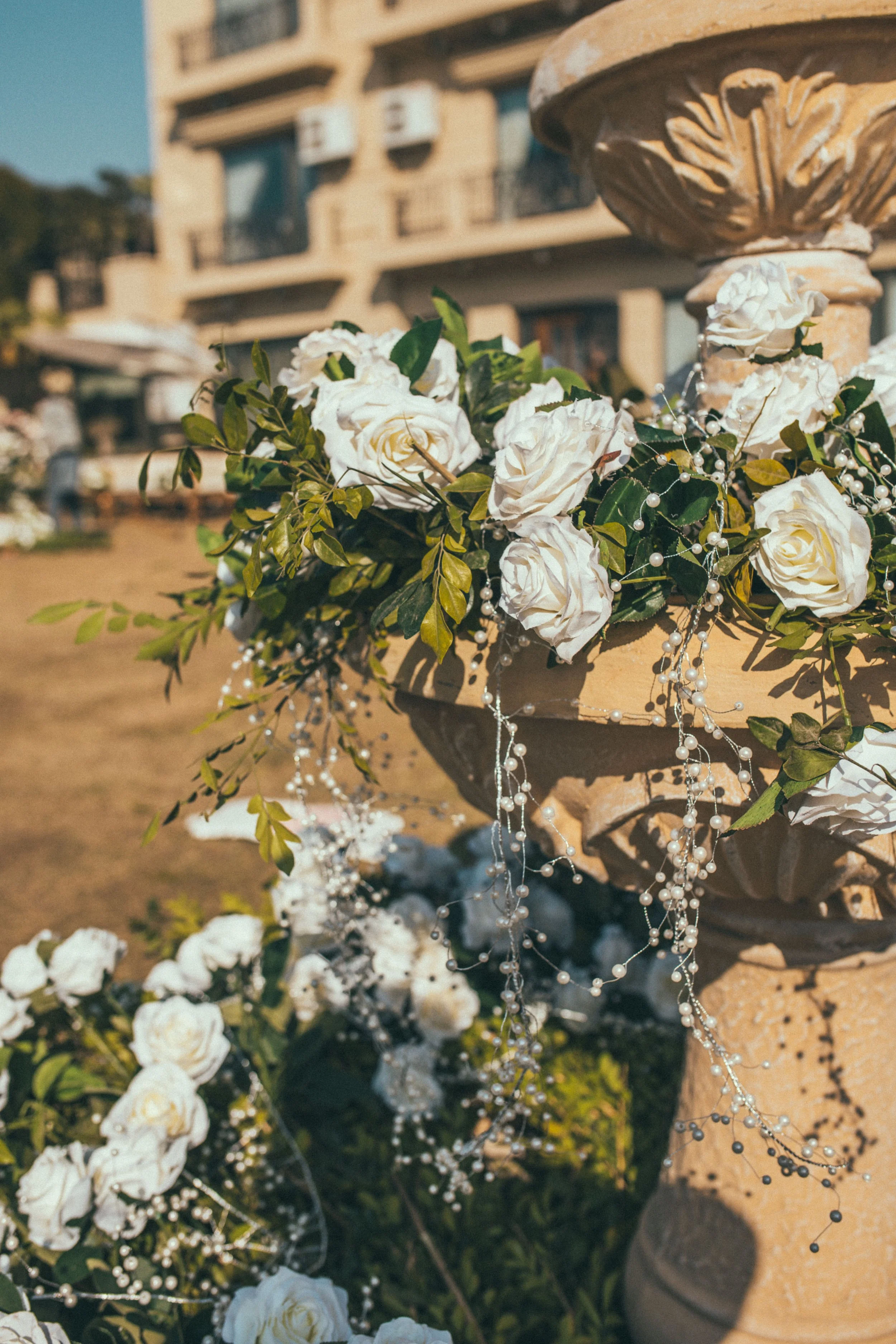 Decorative stone fountain adorned with white roses and beads in an outdoor setting.