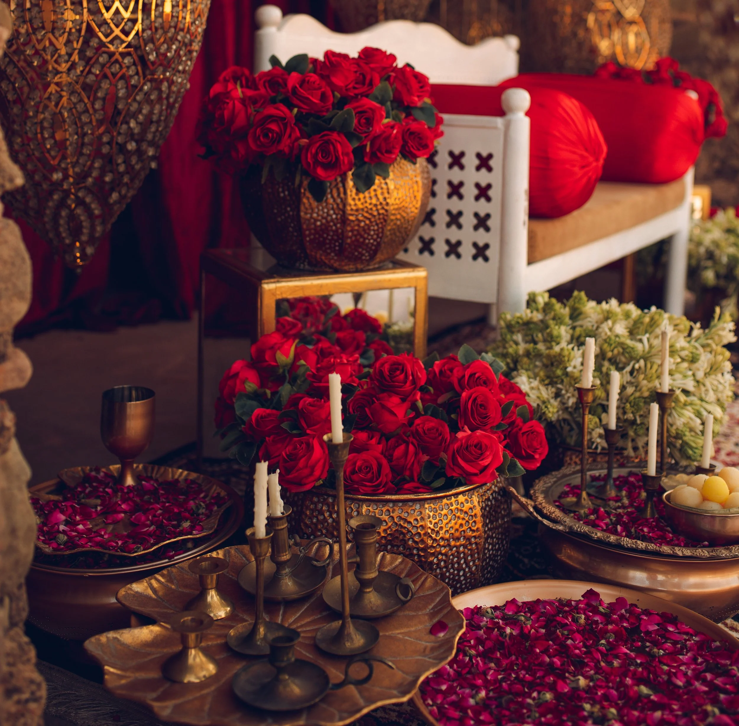 Elegant decor with red roses, metal vases, brass candle holders, and red cushions on a white chair, creating a luxurious and romantic ambiance.