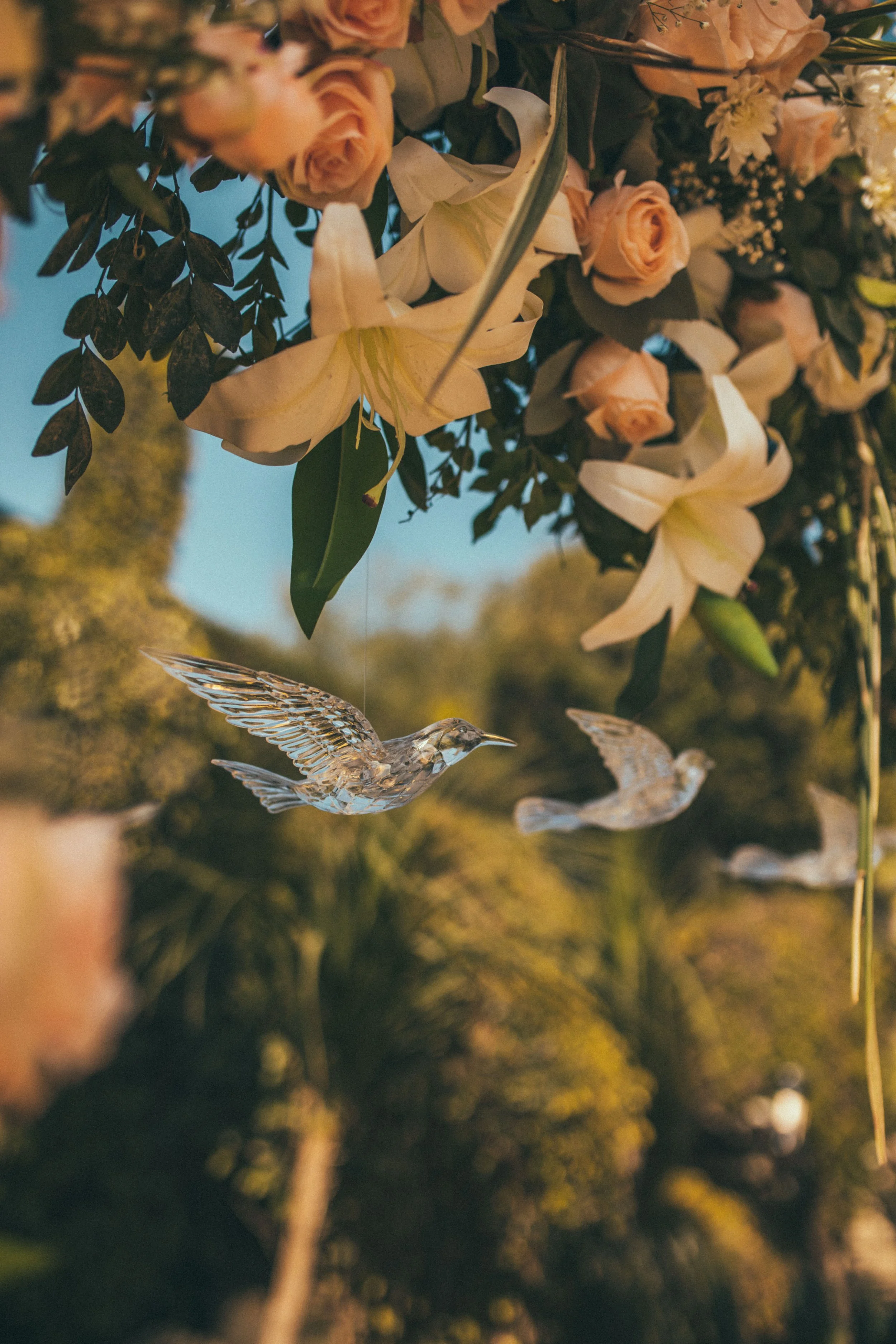 Hanging glass birds with pink roses and white lilies in a garden setting
