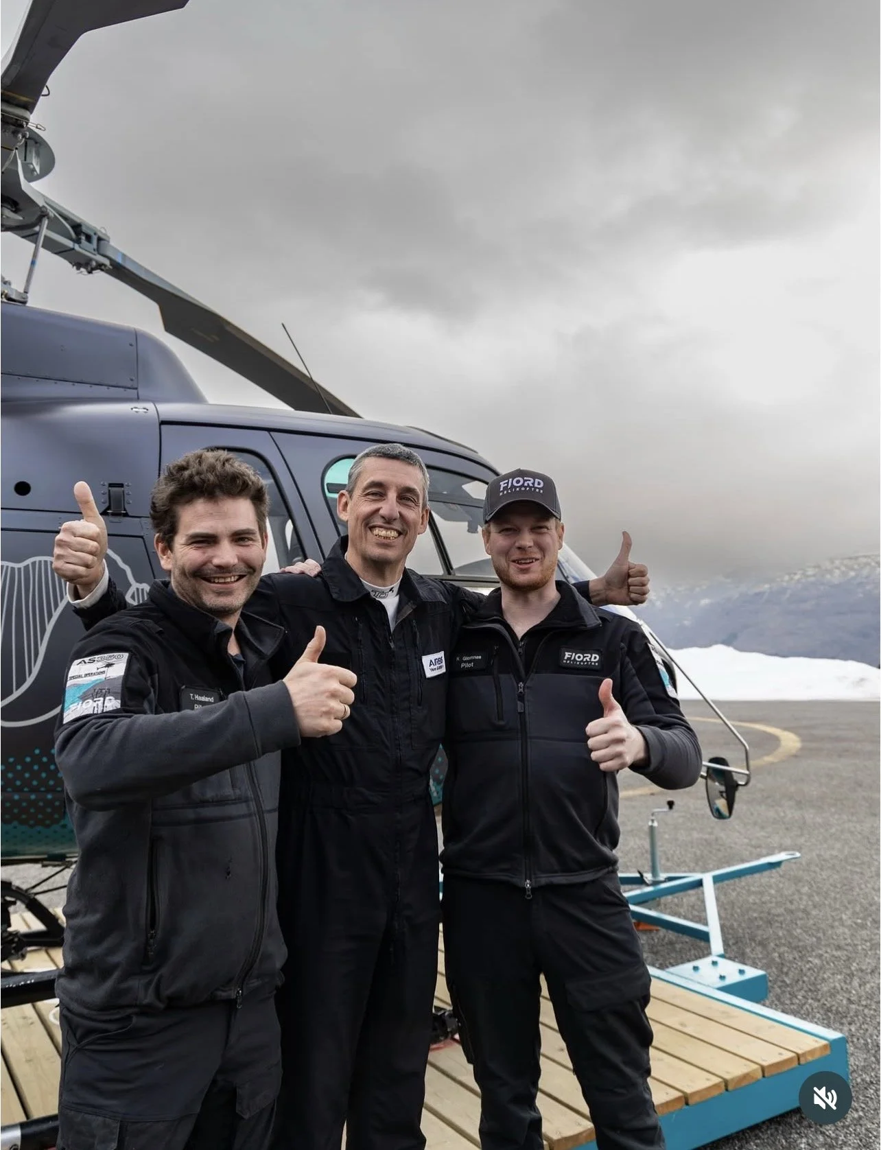 3 menn med tommel opp og smil foran et fjord helikopter