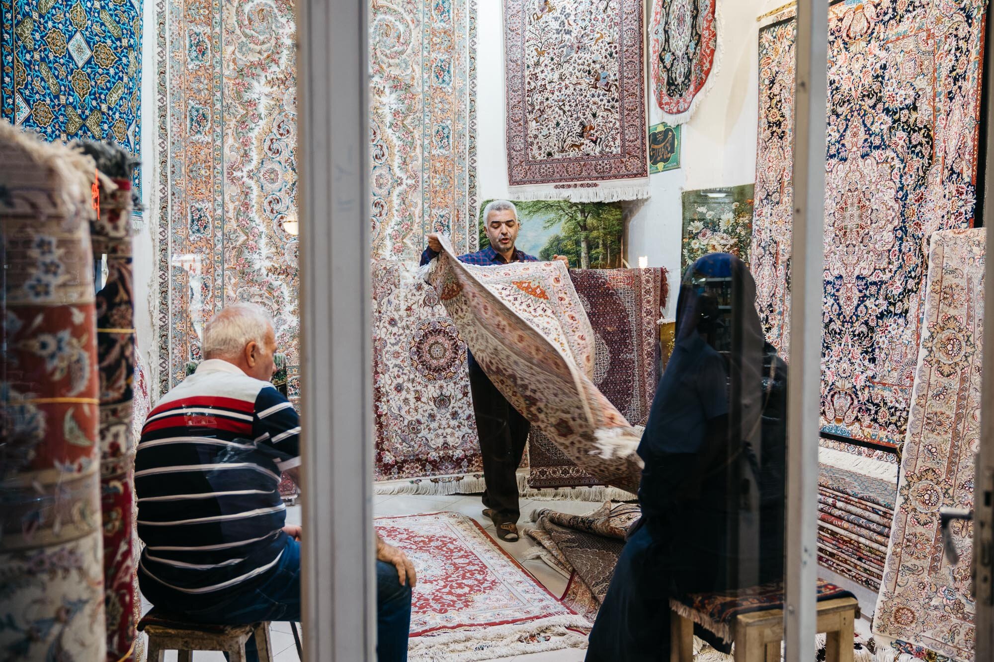  A carpet seller displaying a rug to potential buyers. He is showing off fine silk carpets. 