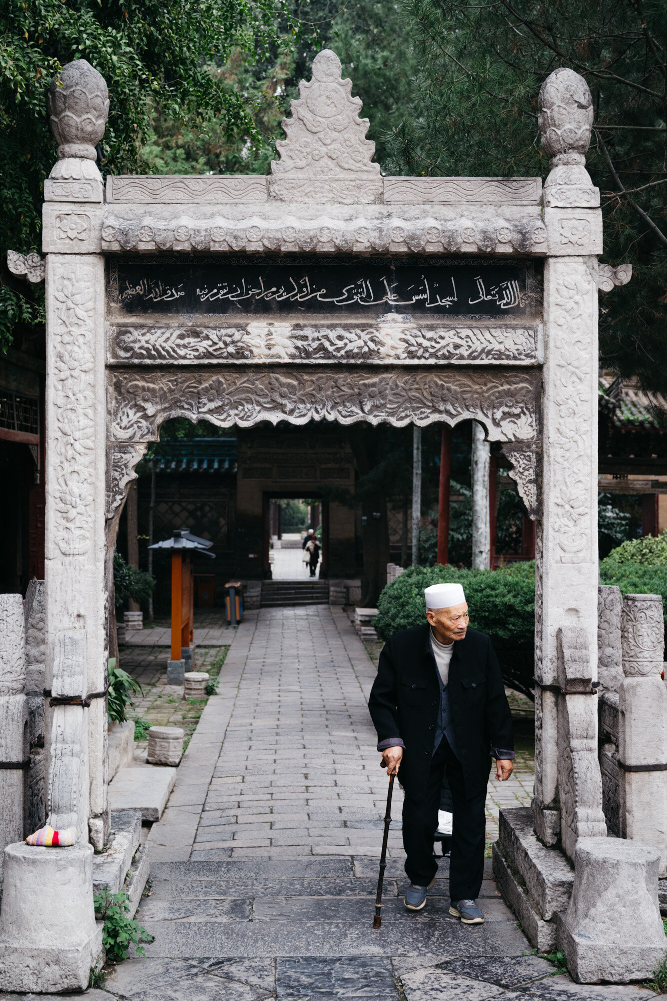  A man heeding the call to prayer. Arabic script can be seen on the gateway he walks through. 