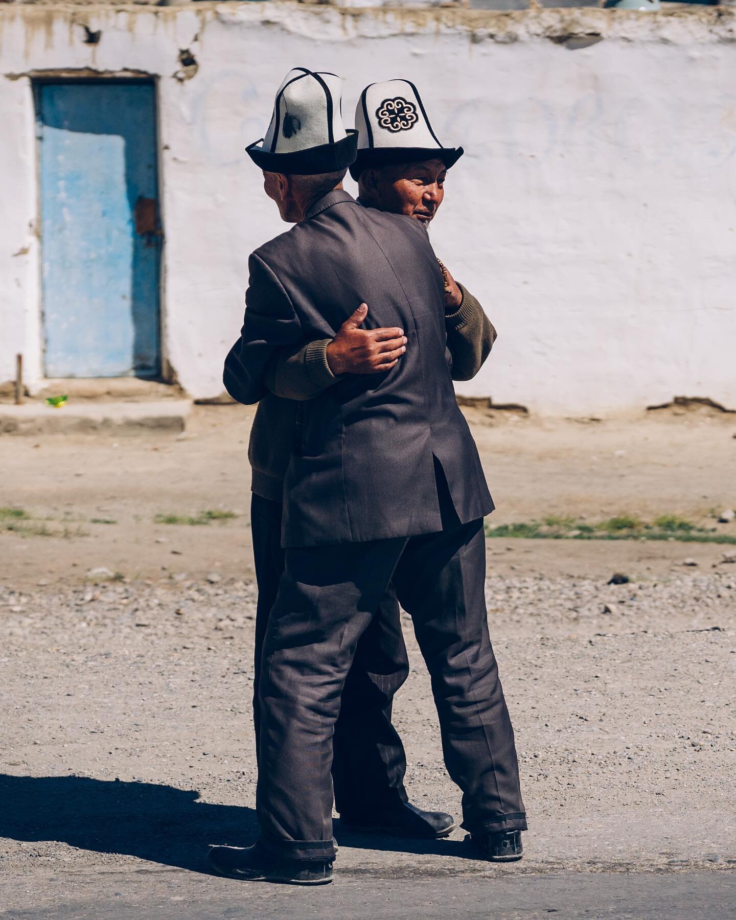 Two friends embrace on the streets of Murghab in eastern Tajikistan, the highest and probably the most remote town in the country. They both wear traditional kalpak hats suggesting they are Kyrgyz men. Semi nomadic communities from Kyrgyzstan will cr