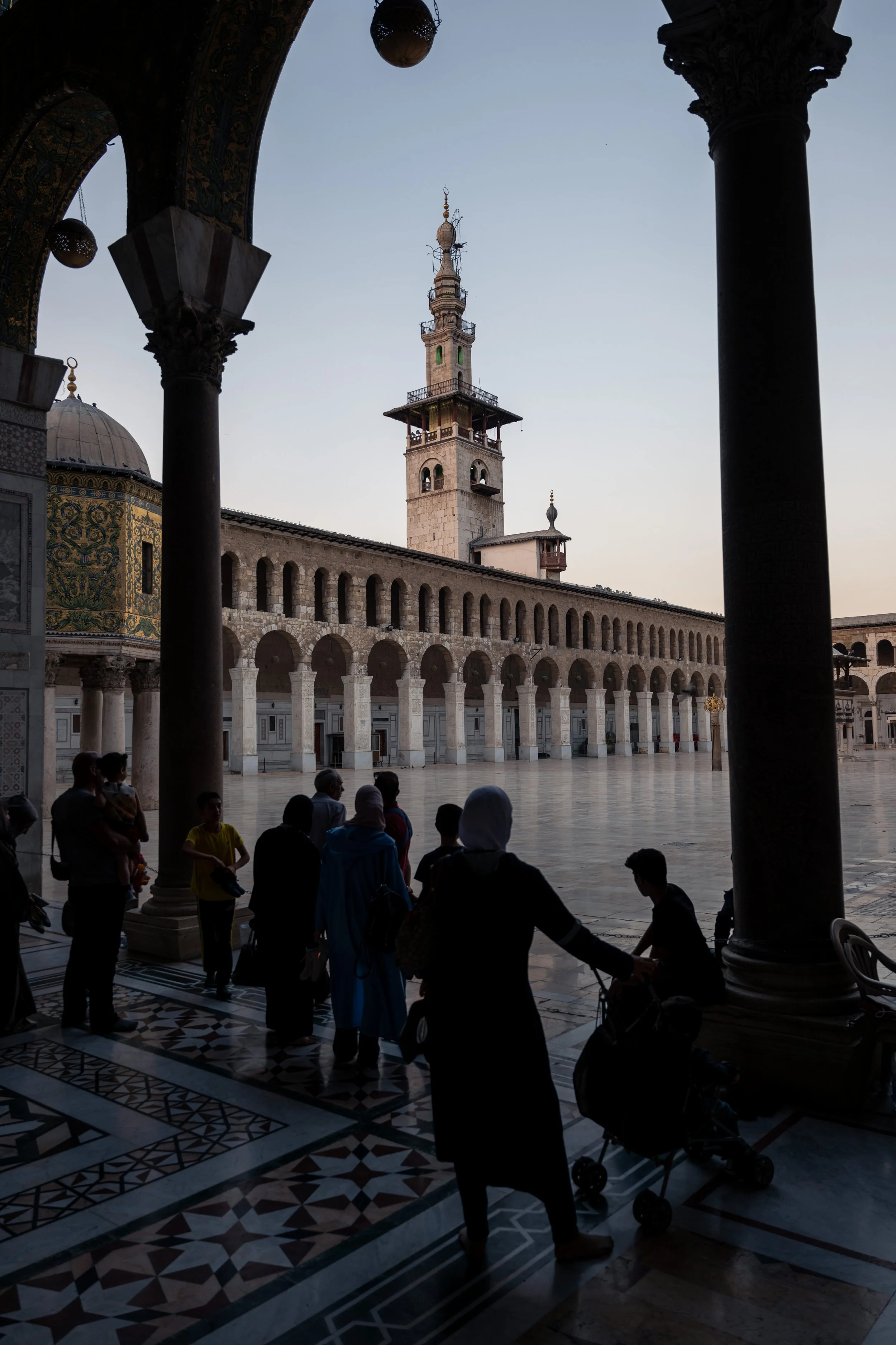  People gather in around the courtyard with the Minaret of the Bride beyond them. 