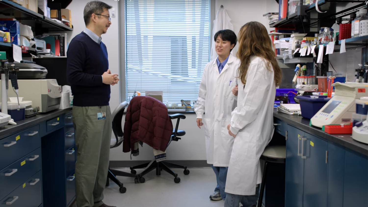 Wang (left) engages with two students in a Johns Hopkins lab. Photo still from Johns Hopkins Biochemistry and Molecular Biology Department video.