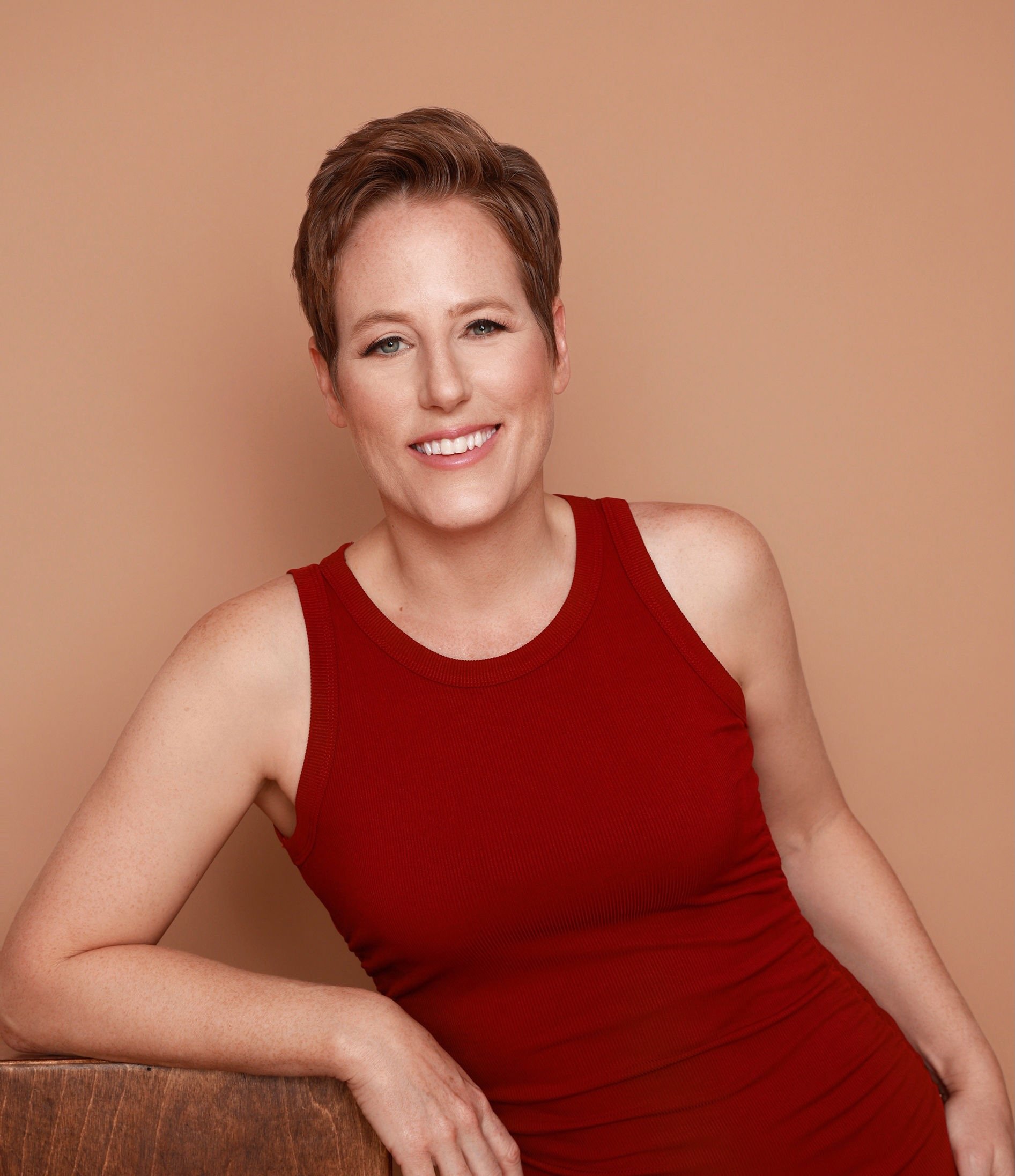 Marisa Nelson, an estate planning attorney in California, a woman with short reddish hair, wearing a red sleeveless top, sitting and smiling at the camera against a beige background.