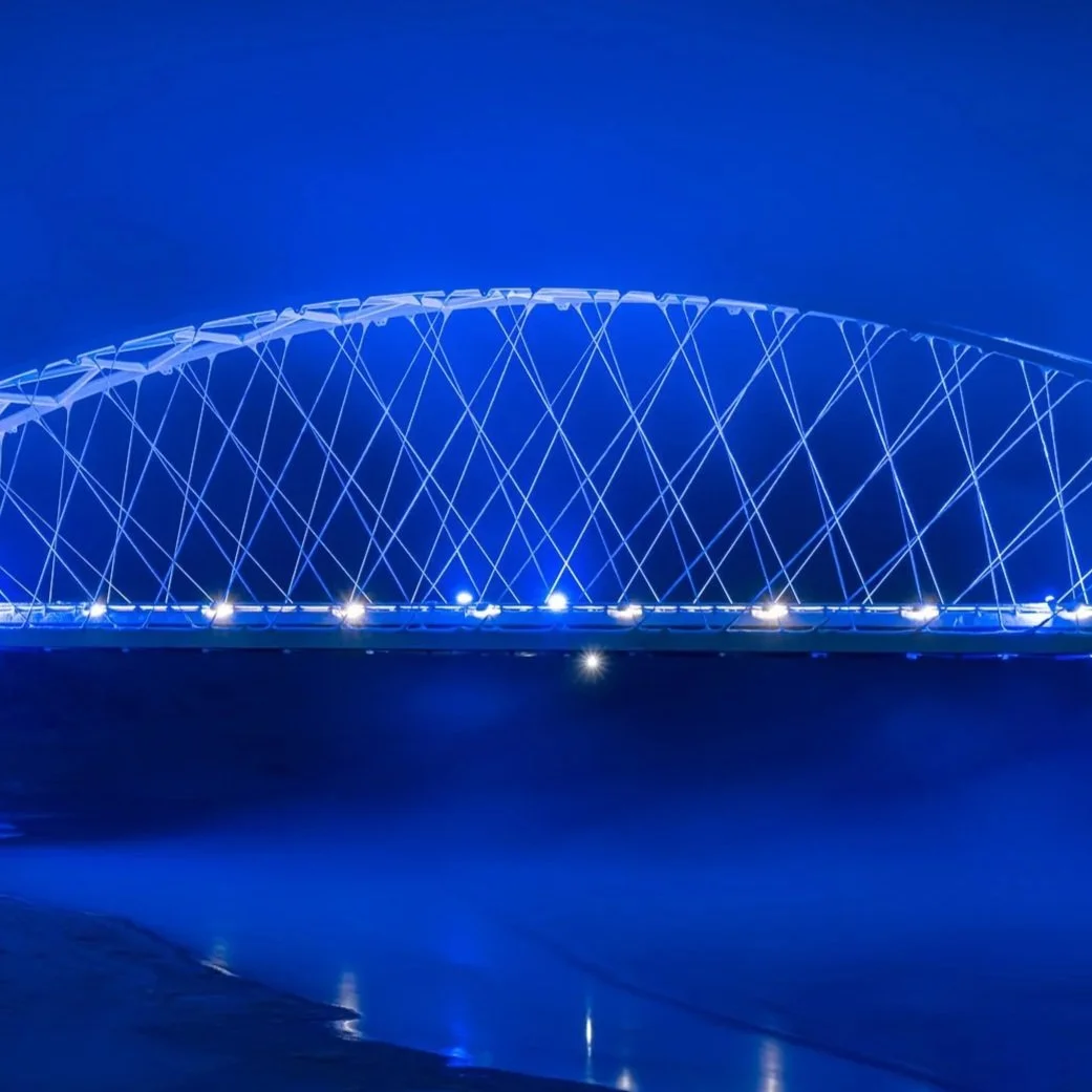 Lite blått opplyst modern bro med en halvsirkel form over vann.
