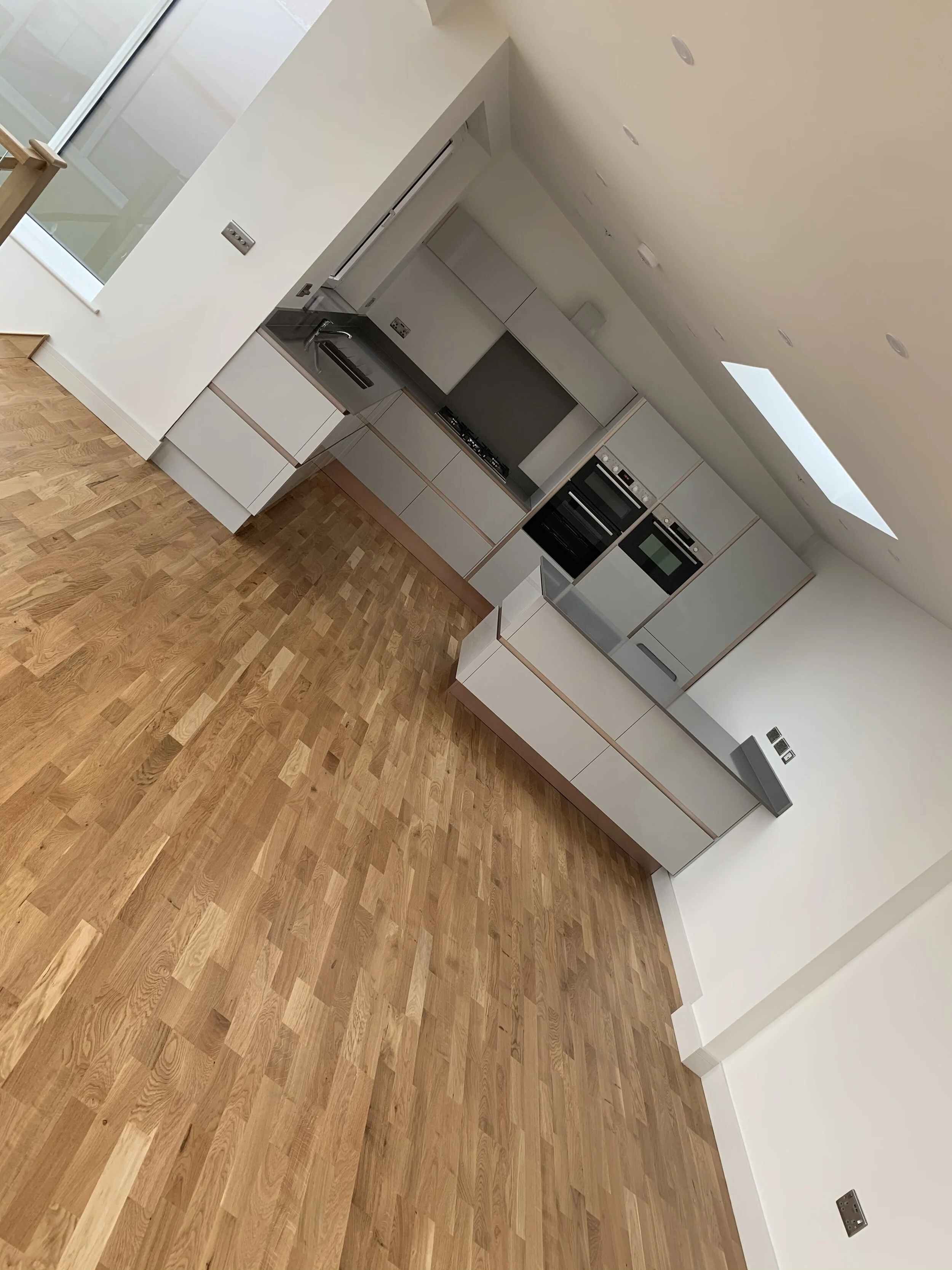 Modern kitchen with white cabinets, built-in oven and microwave, black countertop, gas stovetop, stainless steel sink, wooden flooring, and skylight.