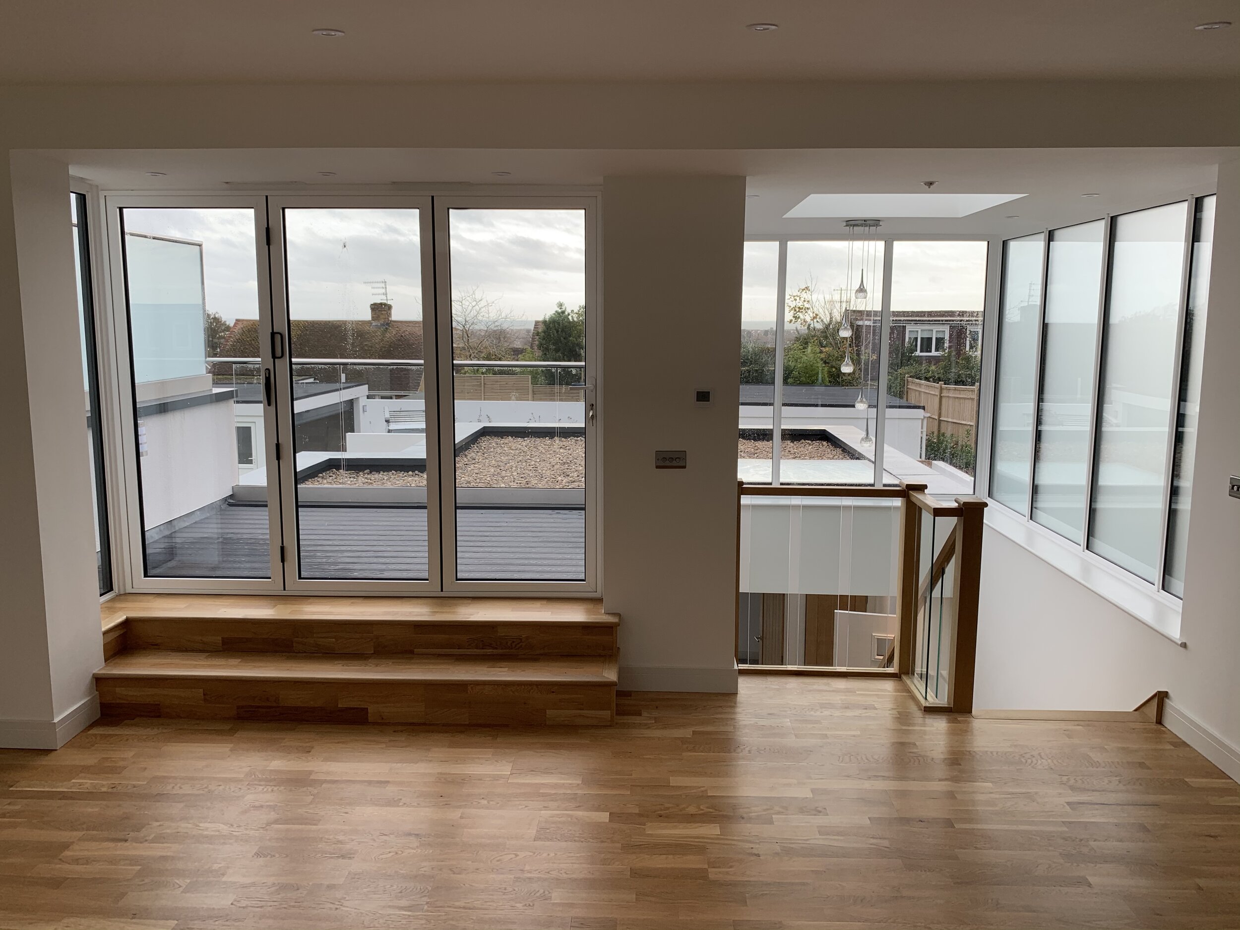 Interior shot of one of our new build projects in North Lancing. A modern new build home with hardwood floors, large glass bifold sliding doors leading to a balcony, and oak staircase with glass balustrade.