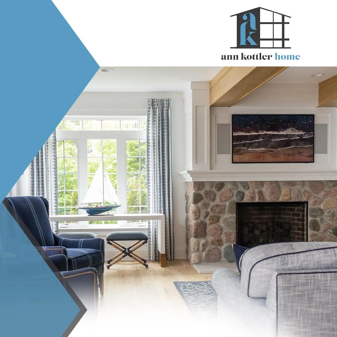 Bright lake house living room with stone fireplace, blue accents, large windows, and a relaxed waterfront-inspired interior design.