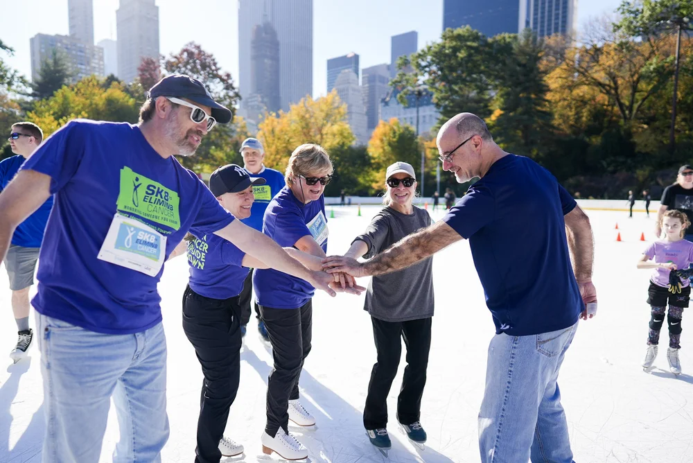 A group of skaters in matching blue shirts on an ice rink during a Sk8 to Elimin8 Cancer charity event for the Scott Hamilton CARES Foundation
