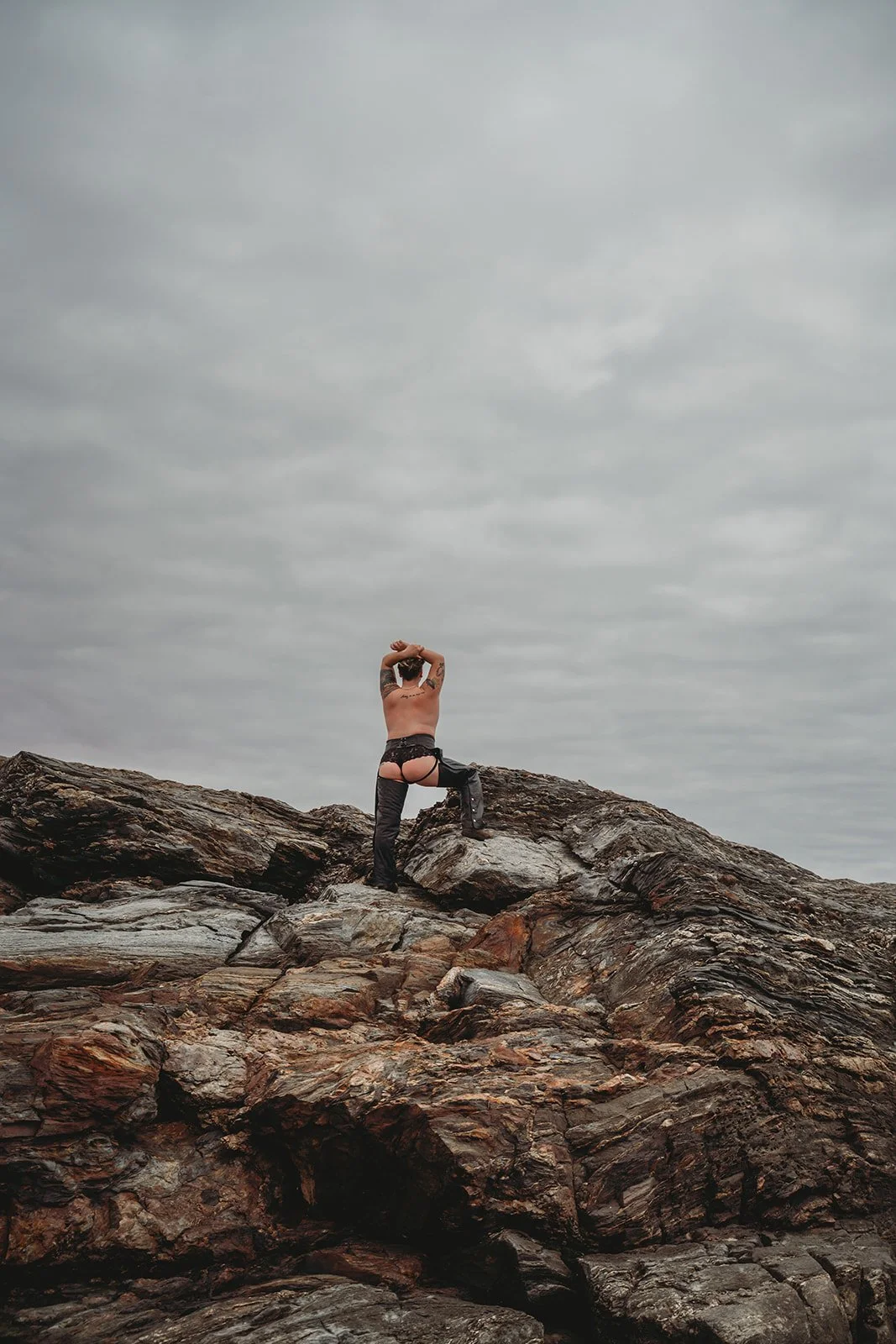 trans nonbinary person wearing assless chaps looking over the ocean