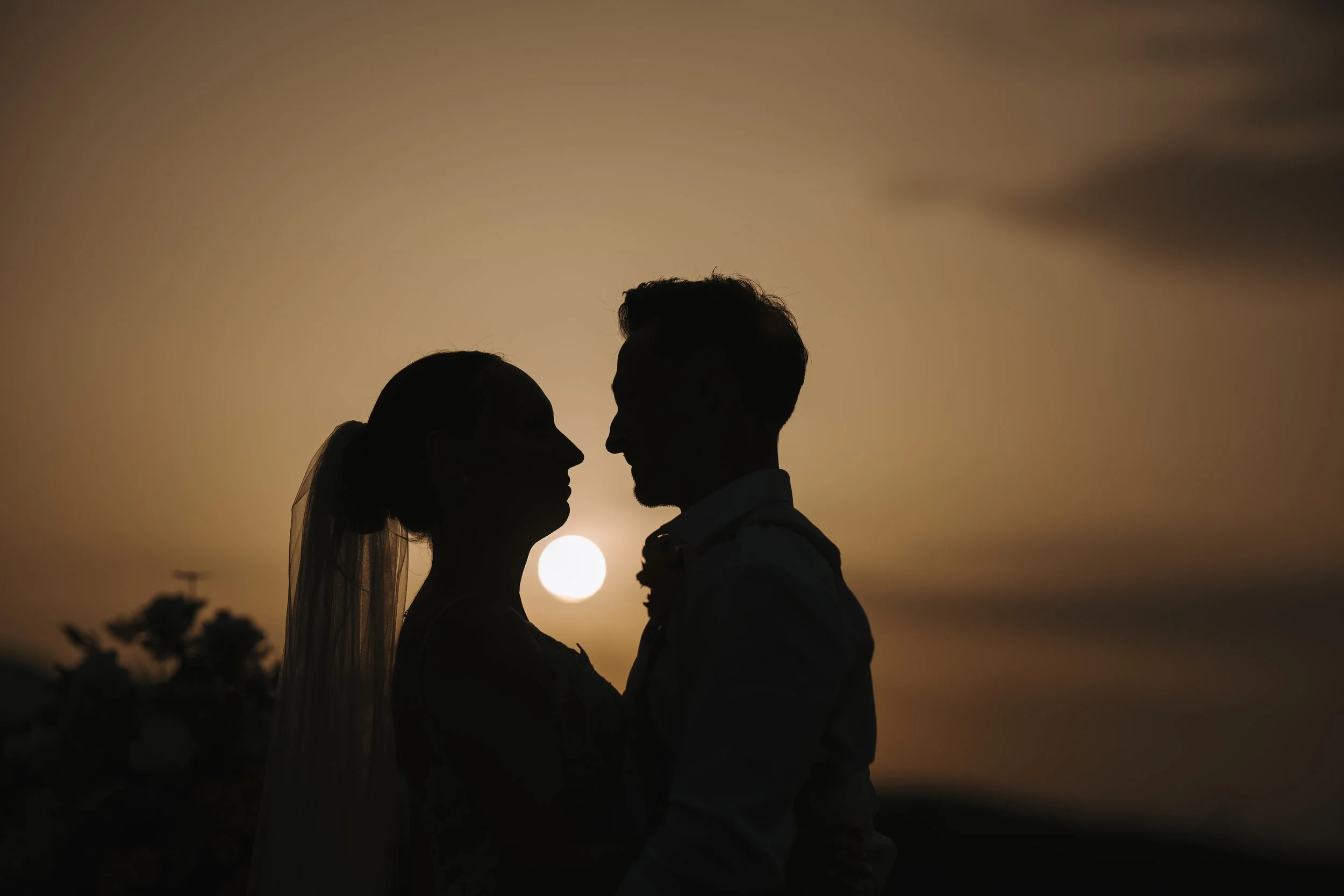 Silhouette of a couple facing each other at sunset, with the sun behind them, creating a romantic scene.