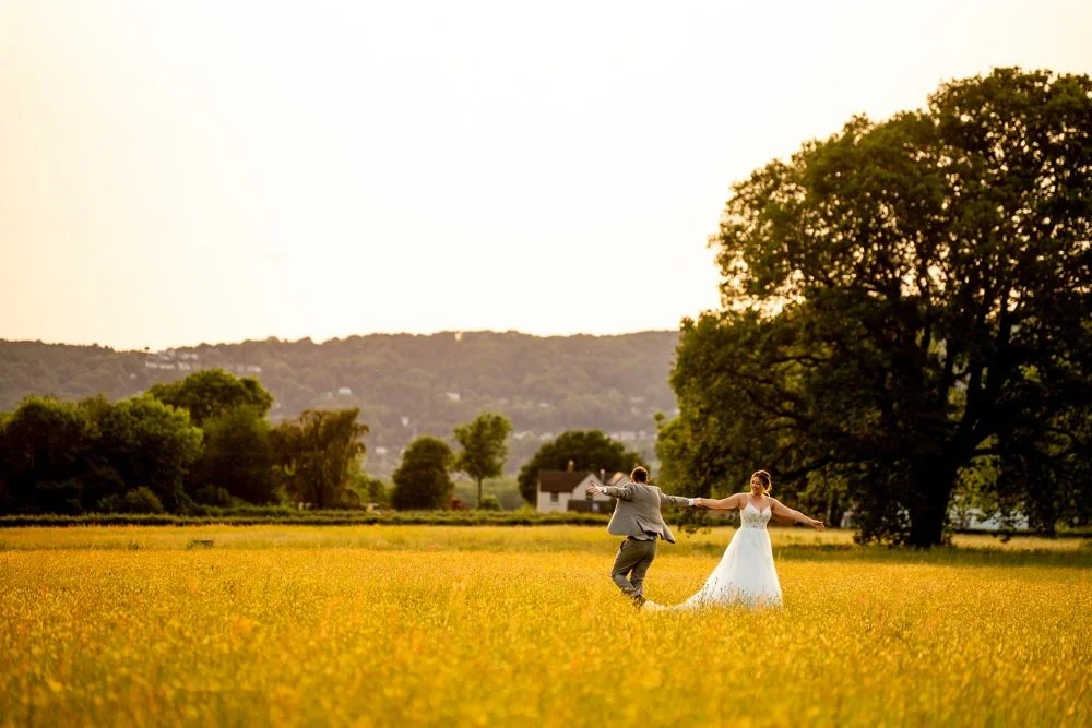 Bride and groom dancing in a yellow field at sunset with trees and a house in the background.