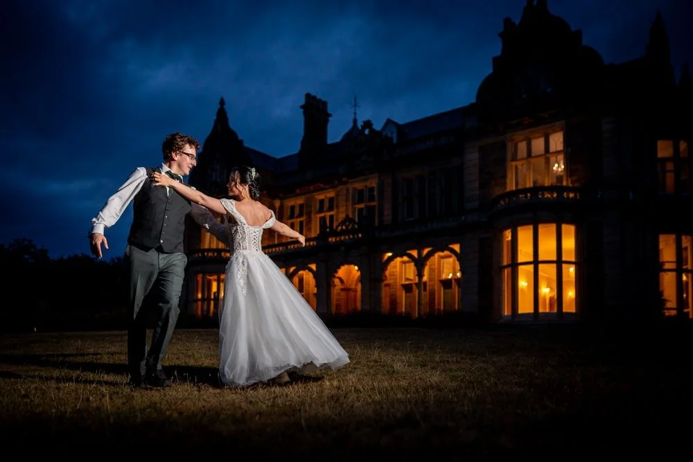 A bride and groom dancing outside a large, illuminated mansion at night.