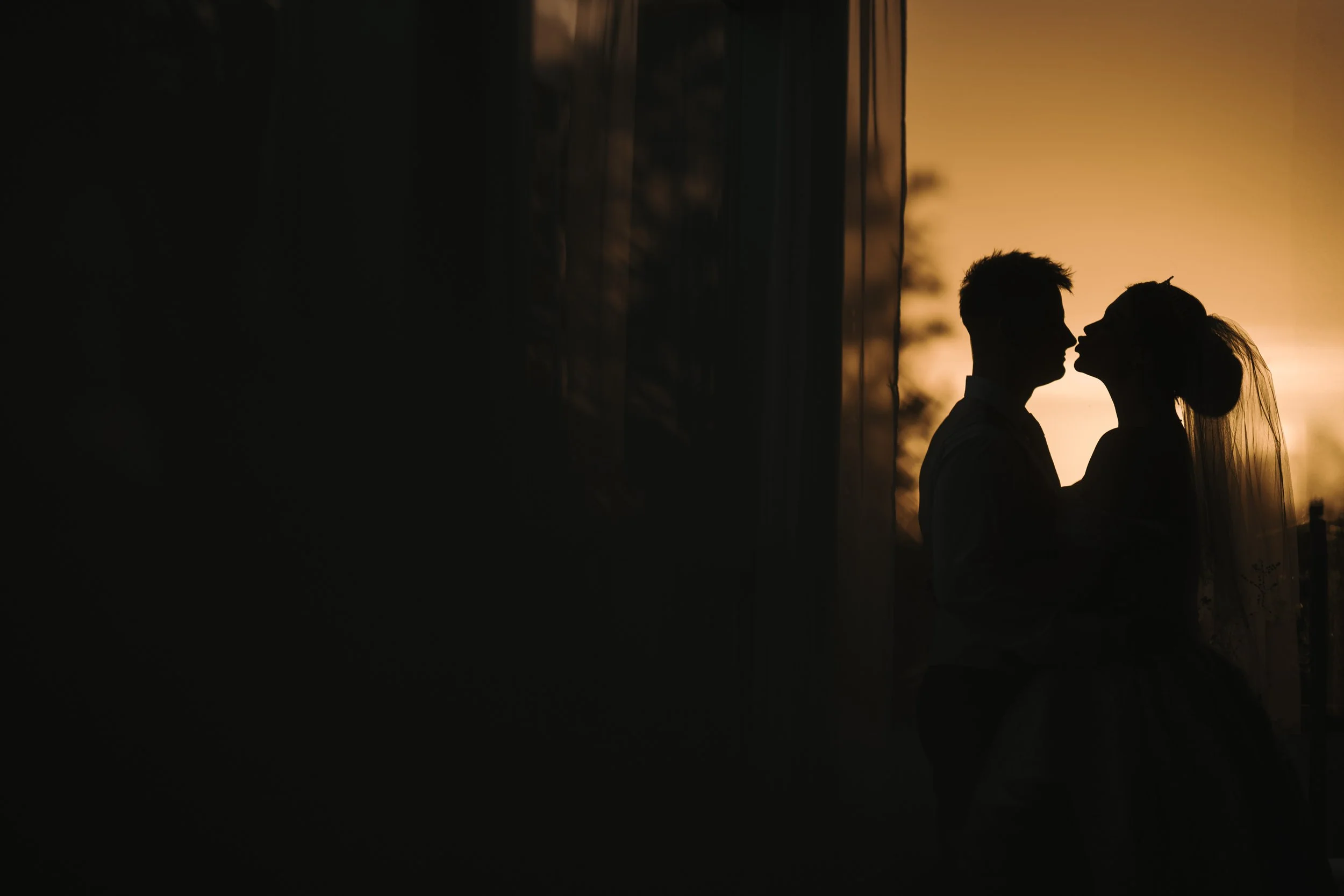 Silhouette of a couple about to kiss during sunset, standing close to each other outdoors.