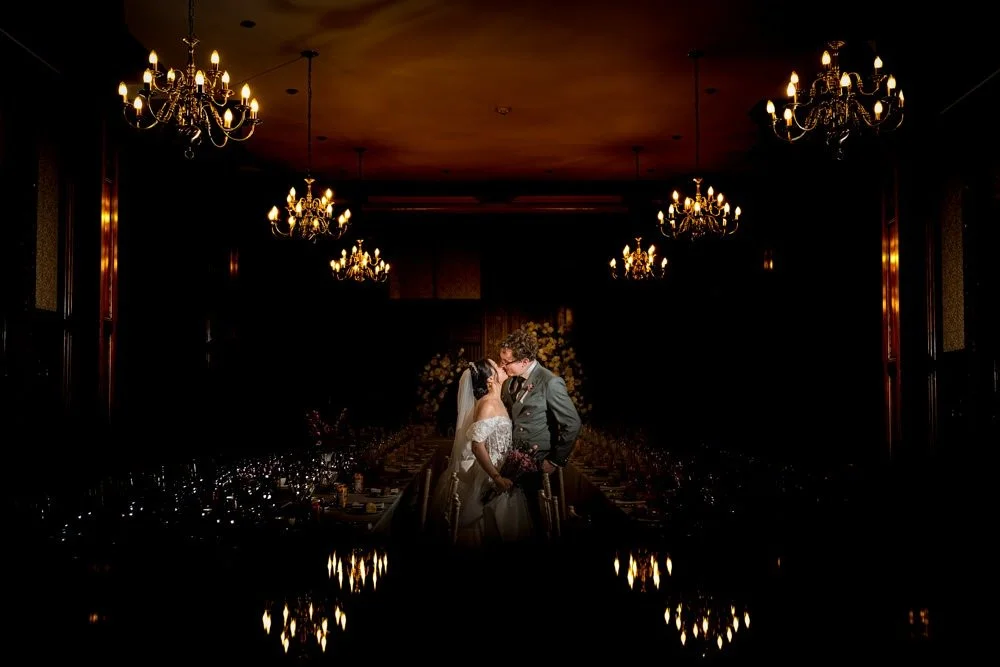 A bride and groom sharing a kiss in a dimly lit room with chandeliers.