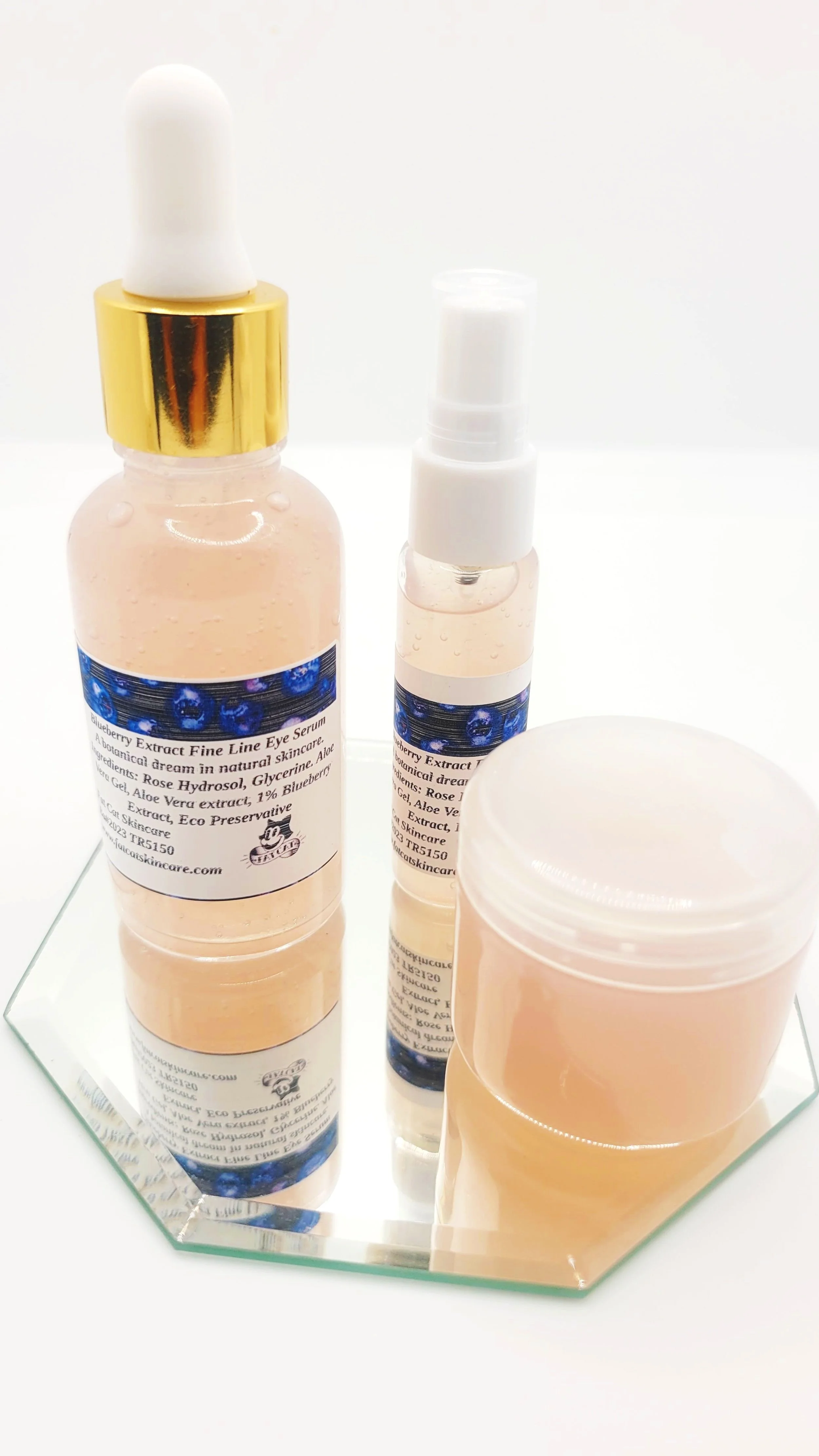 Three skincare products including a serum bottle with a dropper, a spray bottle, and a cream jar on a mirrored surface.