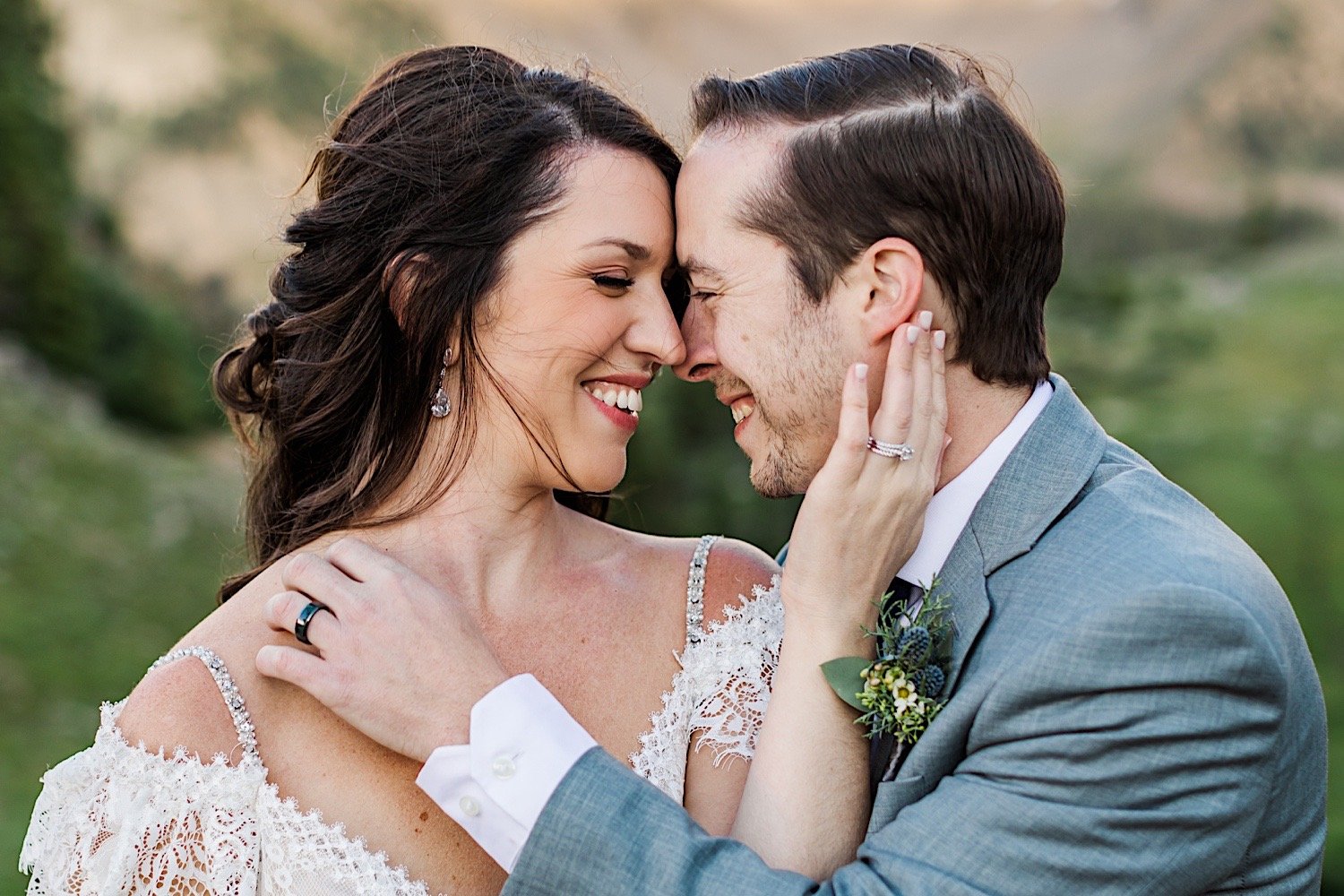 A bride and groom smile at one another as they're about to kiss while showing off their wedding rings