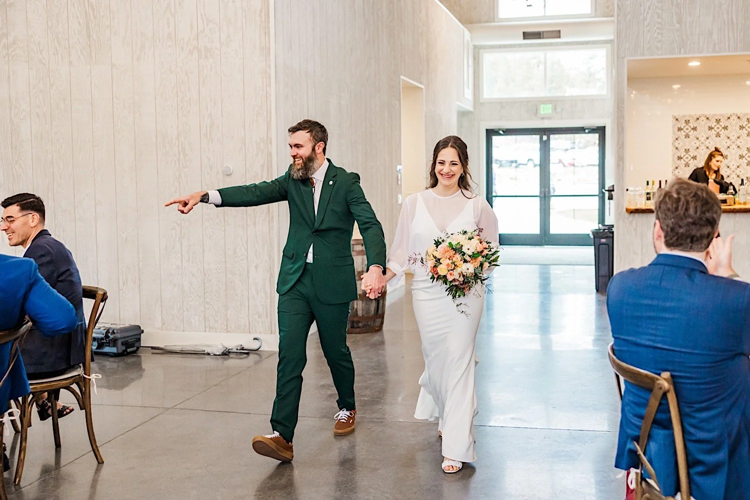 A bride and groom smile while holding hands and walking into their indoor wedding reception at Woodlands Colorado