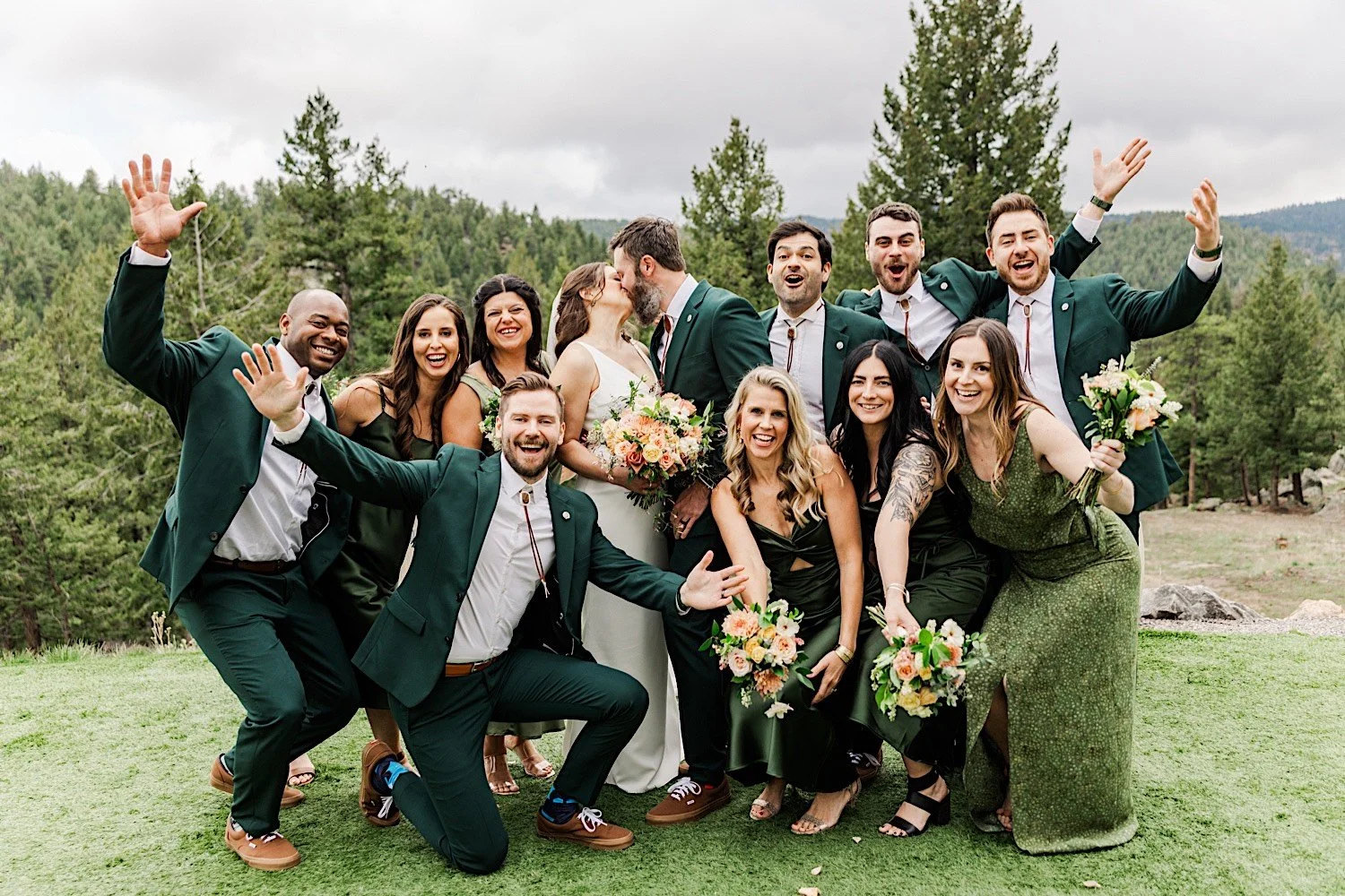 A bride and groom kiss while their wedding party members celebrate around them while outside their wedding venue, Woodlands Colorado