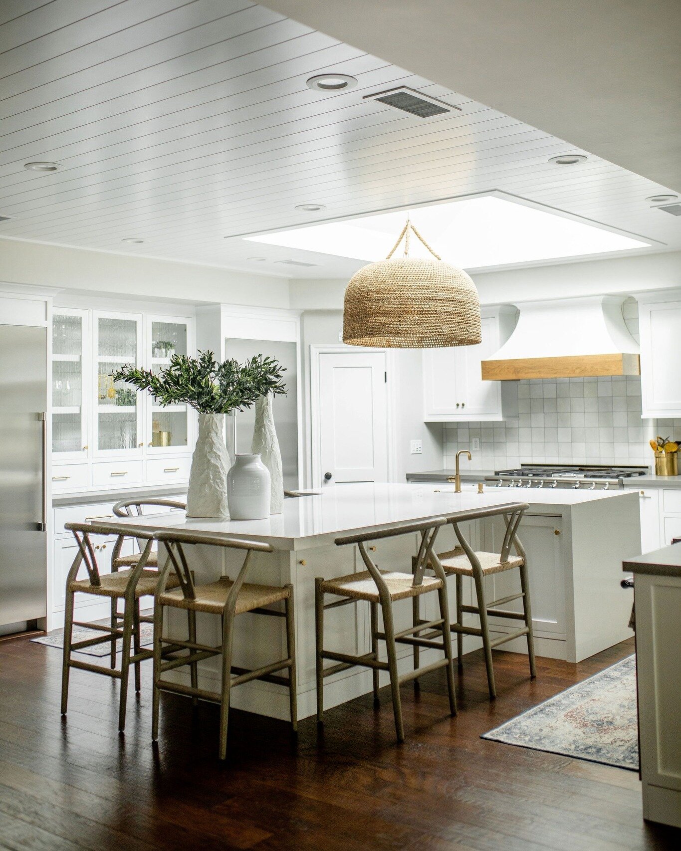 Sunlight streams through the skylight, casting a warm glow on this pristine white kitchen designed by Gracious Living. Clean lines and natural textures create an elegant and calming atmosphere, perfect for culinary creativity. Imagine hosting unforge