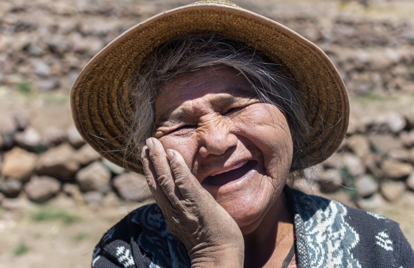 An old woman from Chile wearing a sun hat and holding her hand to her face, wearing a big smile