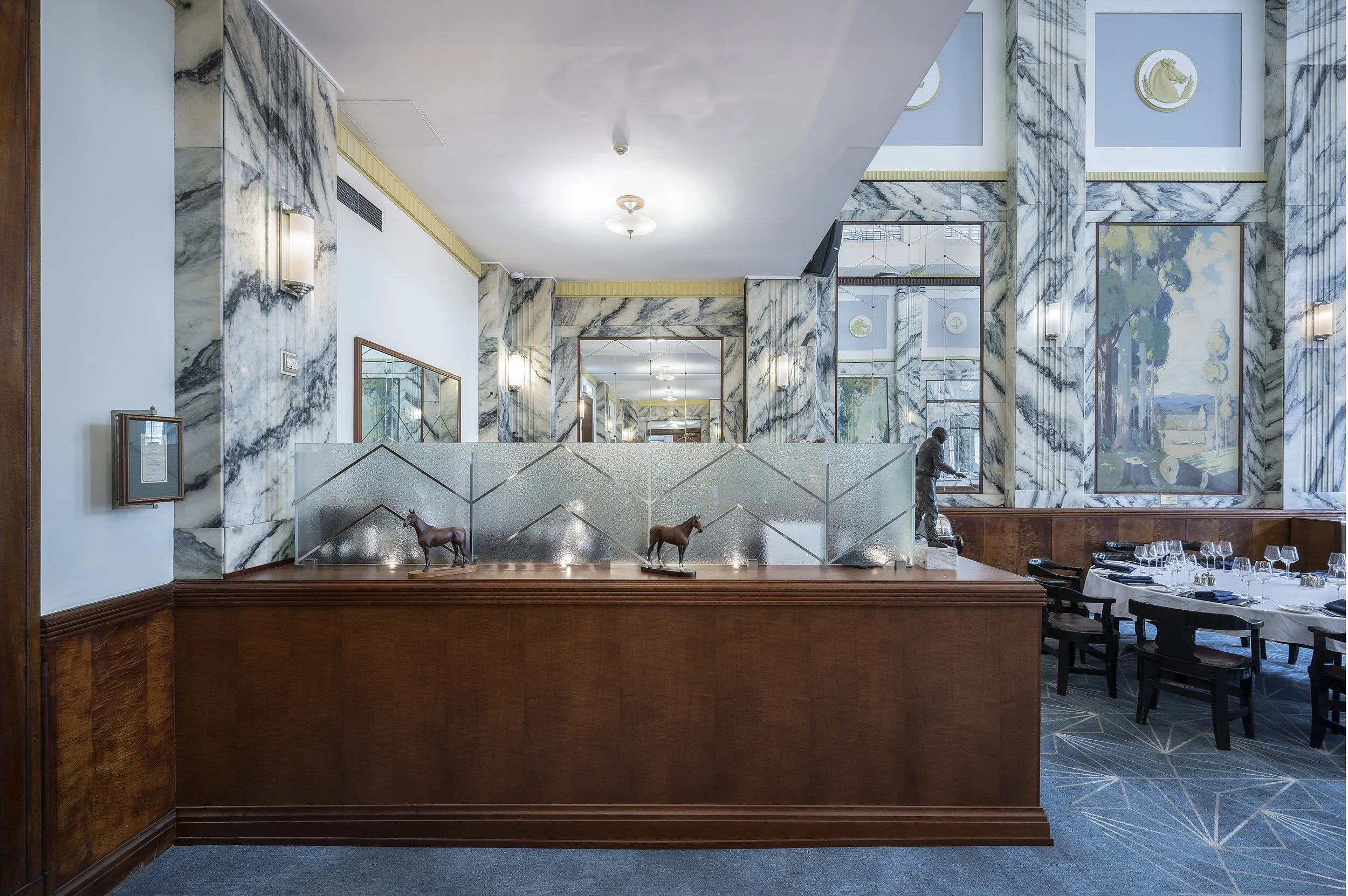 Elegant restaurant interior with marble walls, decorative statues, and set dining tables. Wood paneling and art are featured in the design.