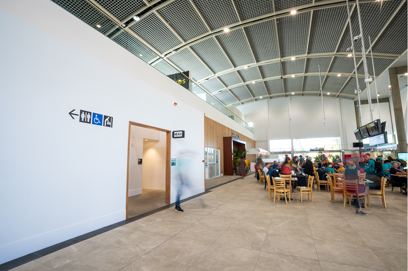 Cairns International T1 Airport. Interior of an airport terminal with restroom signs and a dining area with people sitting at tables. Airport Interior Design Brisbane Australia