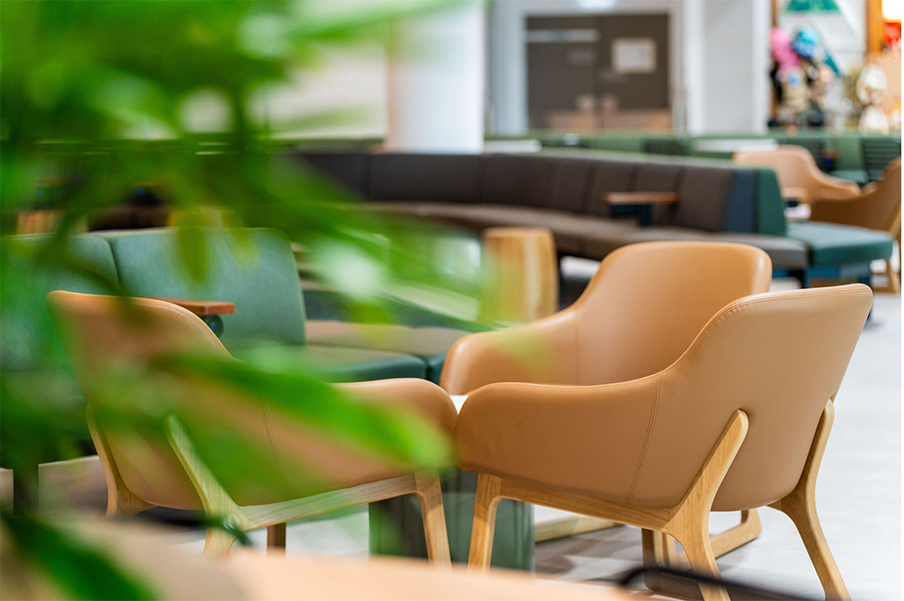 Empty beige armchairs and green couches in a bright, modern lounge or waiting area.